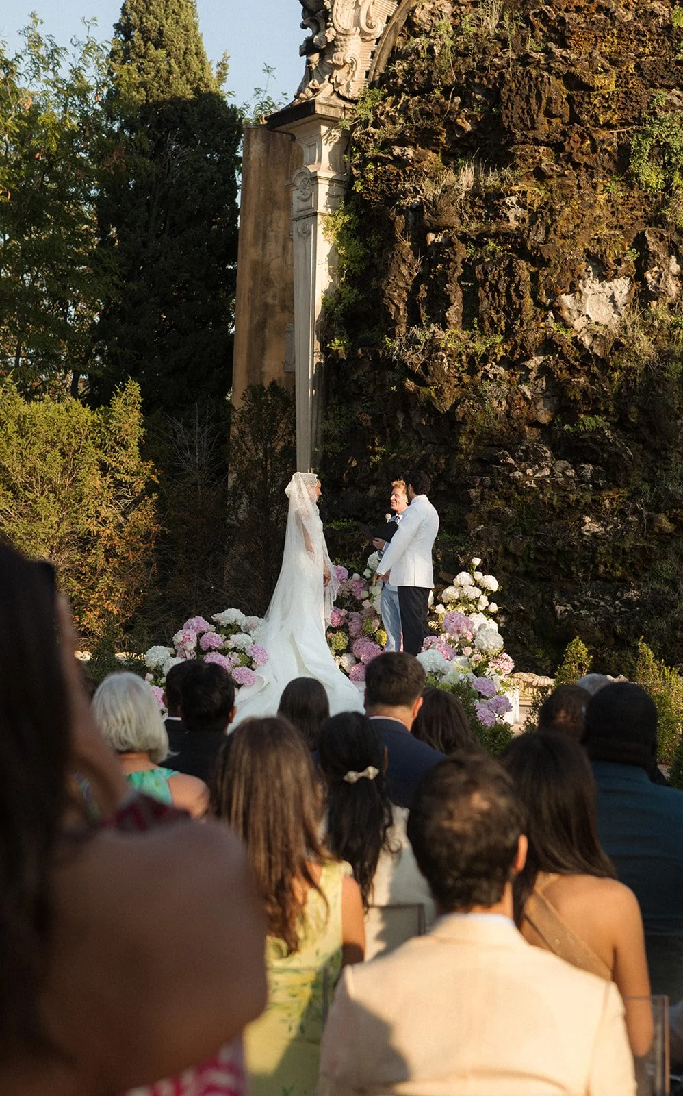 Ceremony at Palácio de Queluz in golden afternoon light with historic stone monument in background, editorial photography by The Lopes Photography