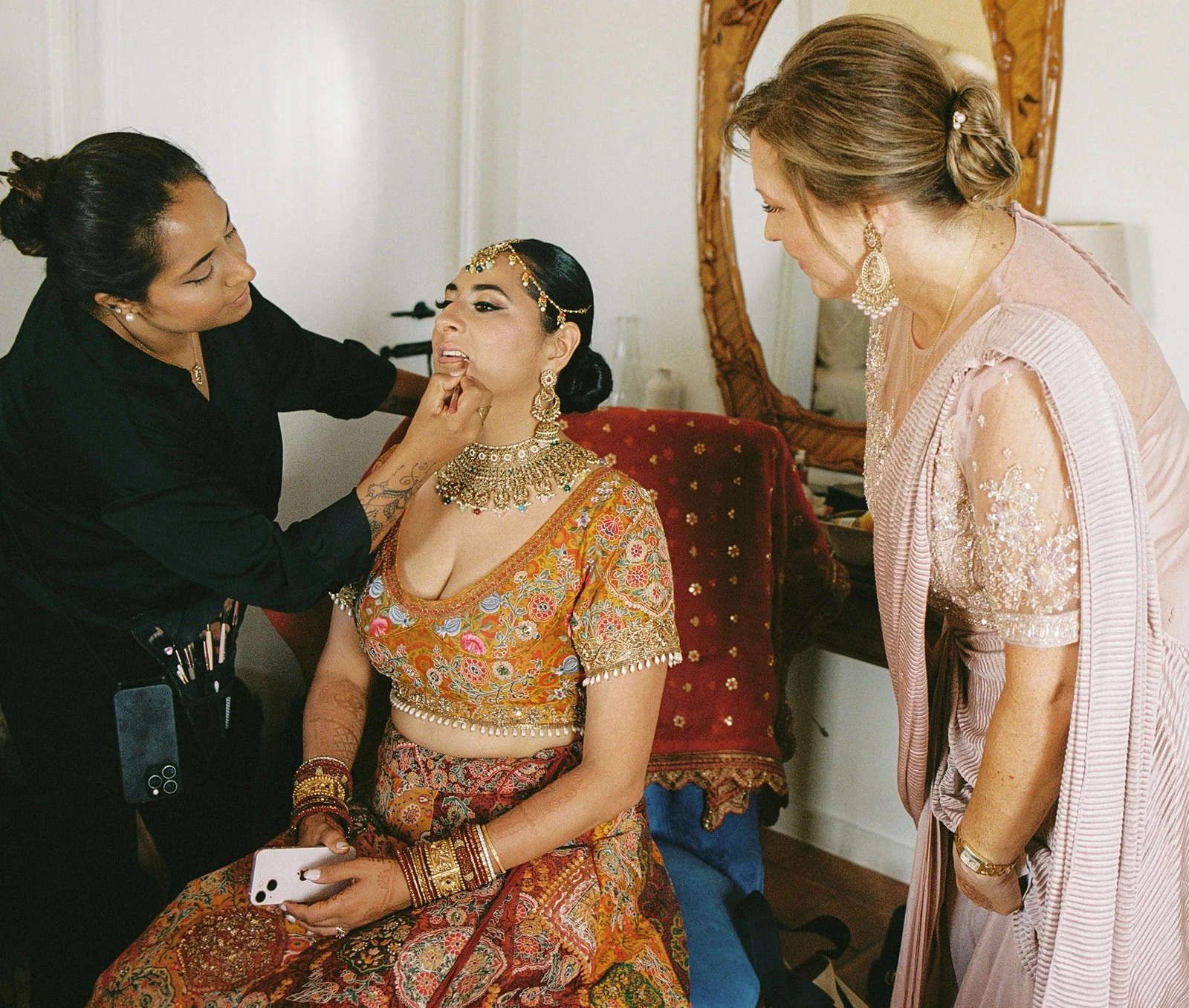 Bride in ornate gold lehenga having makeup applied before a destination wedding ceremony in Portugal | by The Lopes Photography