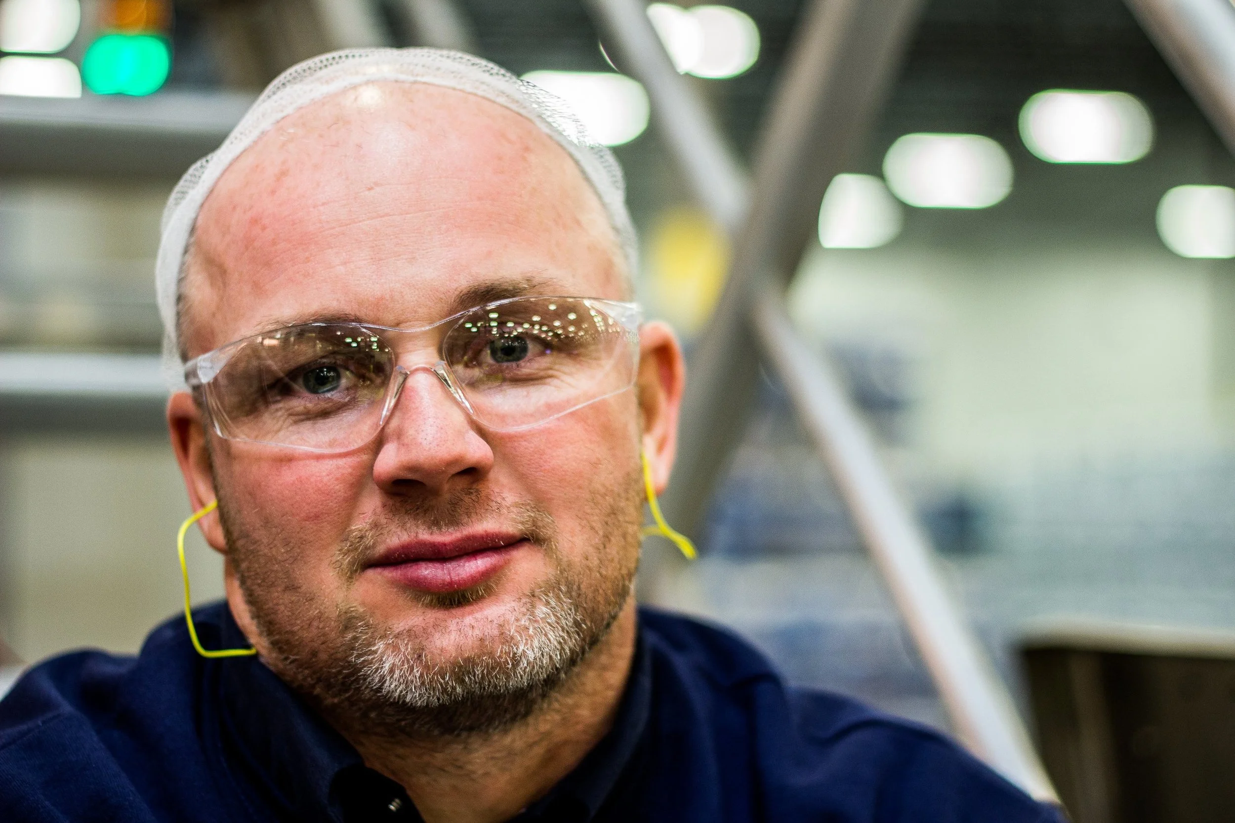 Corporate headshot of a man wearing safety glasses and earplugs in a warehouse setting, commercial headshot photography by Everlux Photo Co.