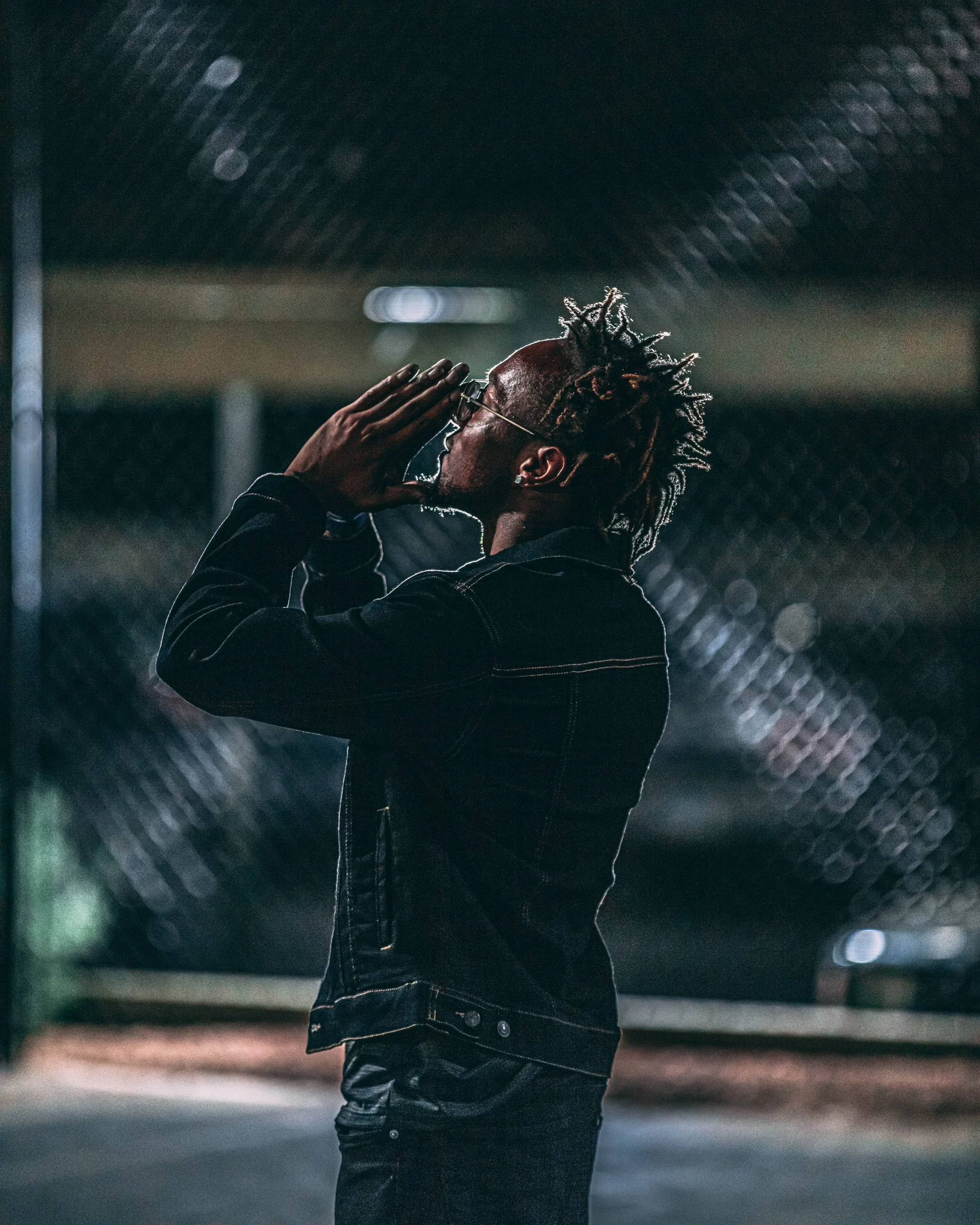 Dramatic nighttime portrait of a man against a chain-link fence with his head tilted upward, portrait photography by Everlux Photo Co.