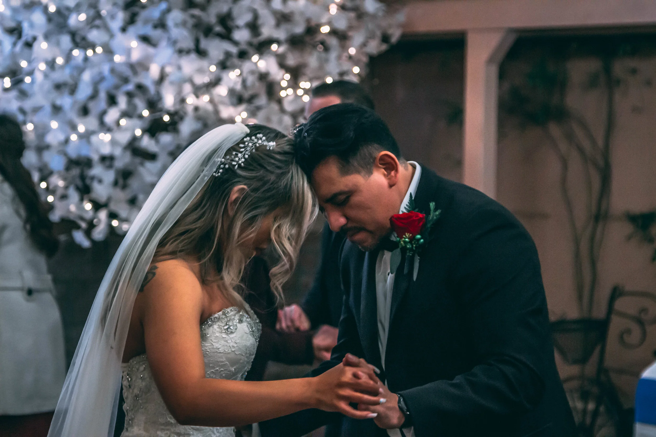 Intimate portrait of a groom presenting a rose to his bride, weIntimate portrait of a bride and groom holding hands under string lights, wedding photography by Everlux Photo Co.dding photography by Everlux Photo Co.