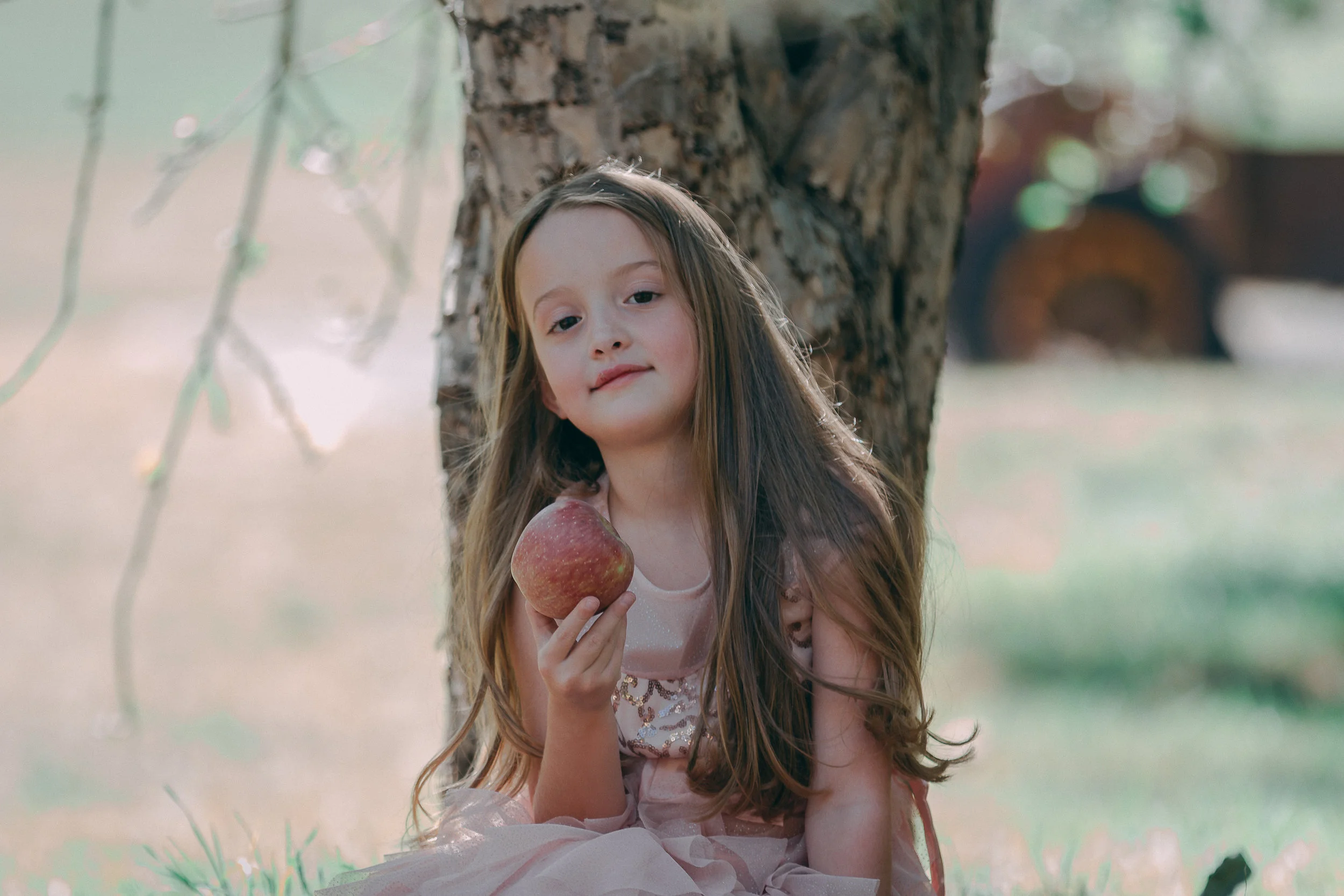 Portrait of a young girl sitting by a tree holding an apple, child photography by Everlux Photo Co.