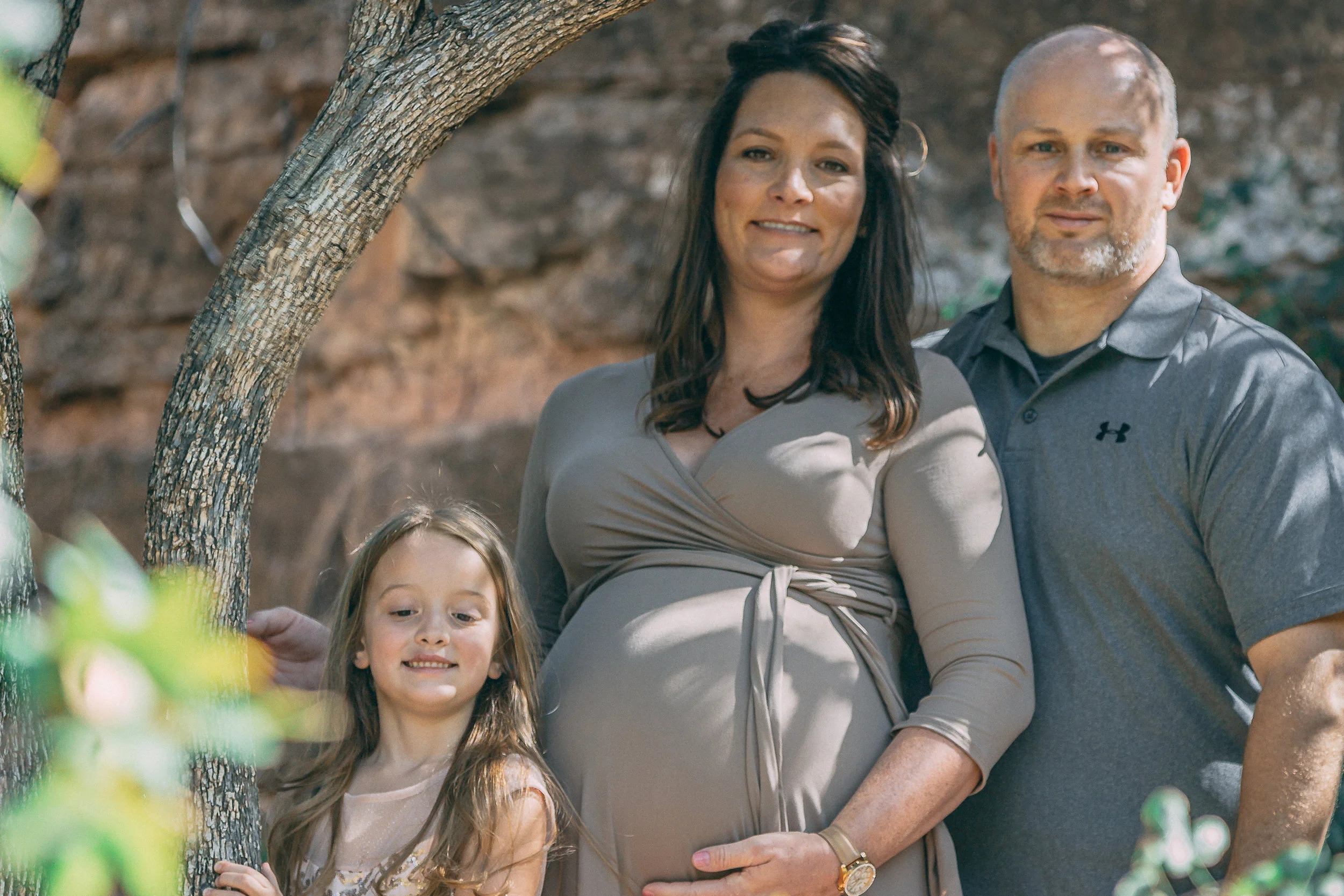 Maternity family portrait of parents and their young daughter against a natural rock backdrop, family photography by Everlux Photo Co.