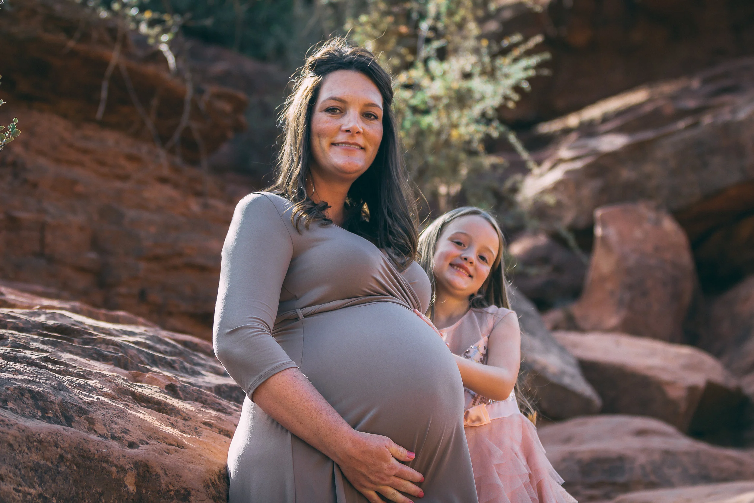 Maternity portrait against red rock formations with young daughter, maternity photography by Everlux Photo Co.