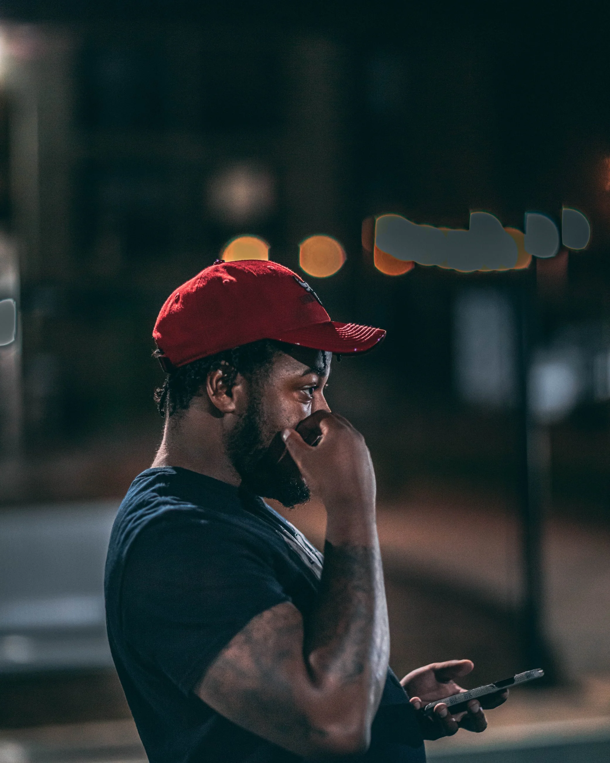 Candid nighttime street portrait of a man in a red cap, urban portrait photography by Everlux Photo Co.