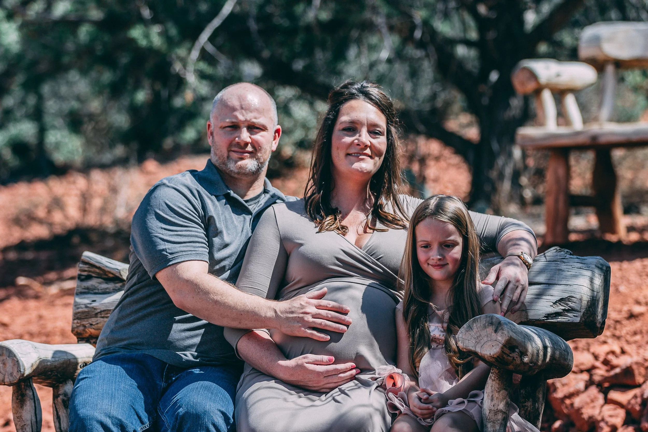 Maternity family portrait of parents and their daughter seated among red rocks, family photography by Everlux Photo Co.