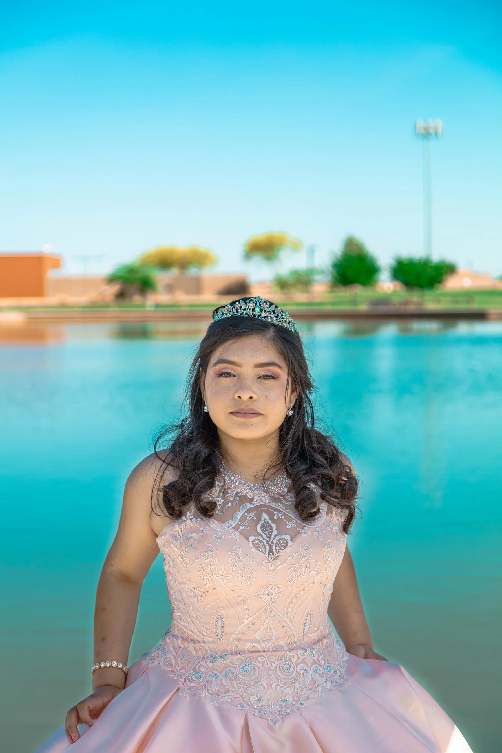 Seated portrait of a young woman in a quinceañera gown and tiara beside a lake, celebration portrait photography by Everlux Photo Co.