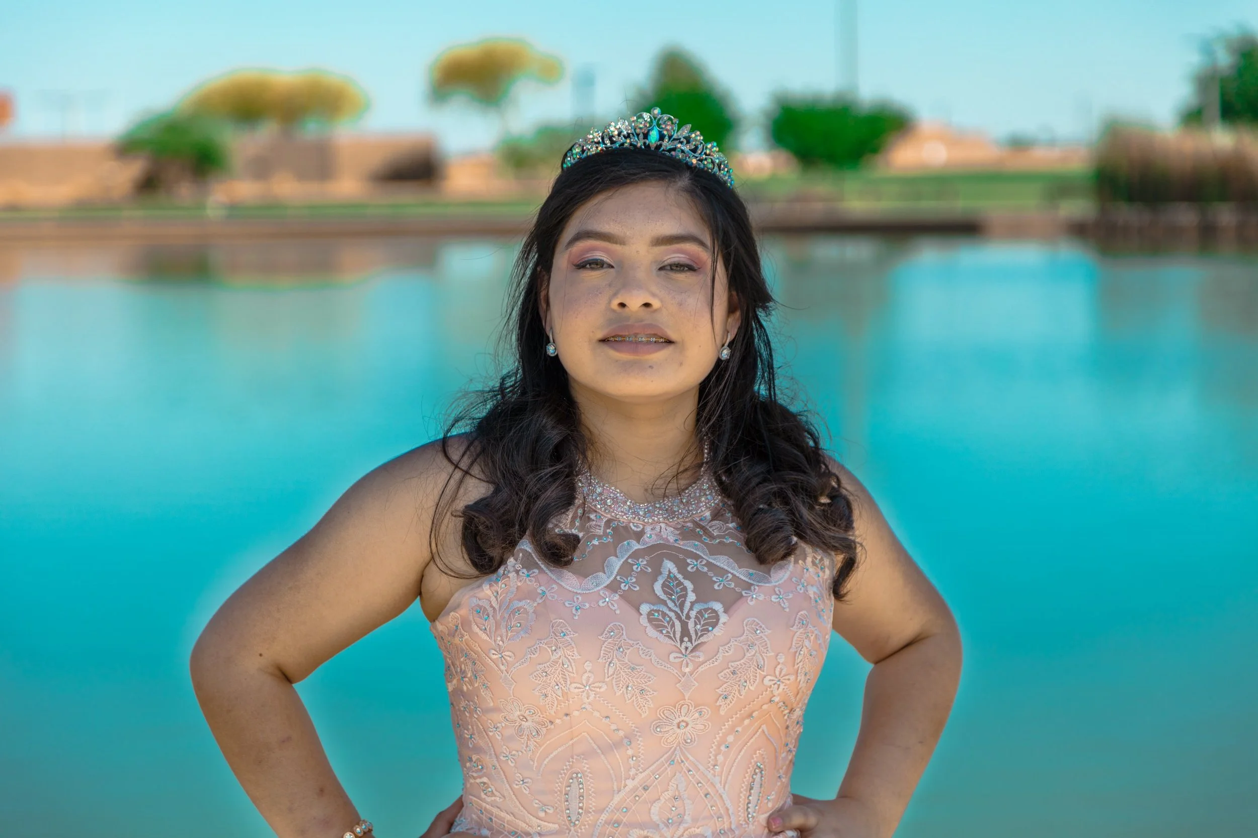 Confident portrait of a young woman in a sparkling quinceañera gown and tiara by the water, celebration portrait photography by Everlux Photo Co.
