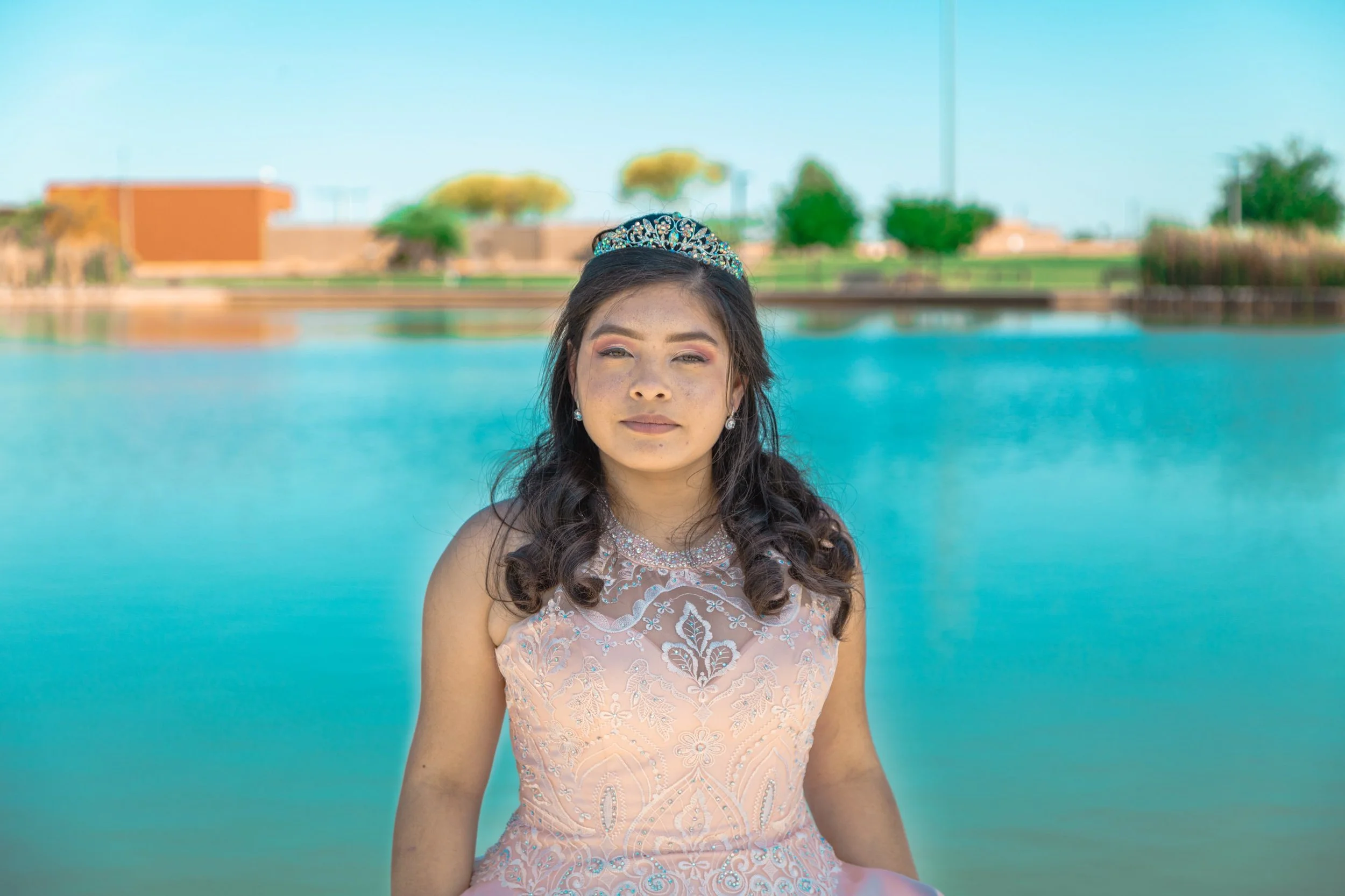 Portrait of a young woman in a sparkling quinceañera gown and tiara against a turquoise lake, celebration portrait photography by Everlux Photo Co.