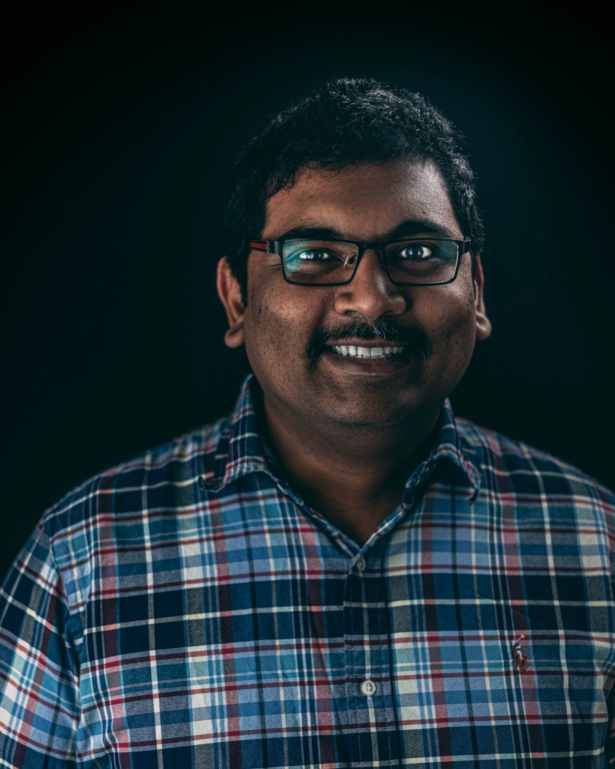 Studio portrait of a smiling man in a plaid shirt and glasses, portrait photography by Everlux Photo Co.