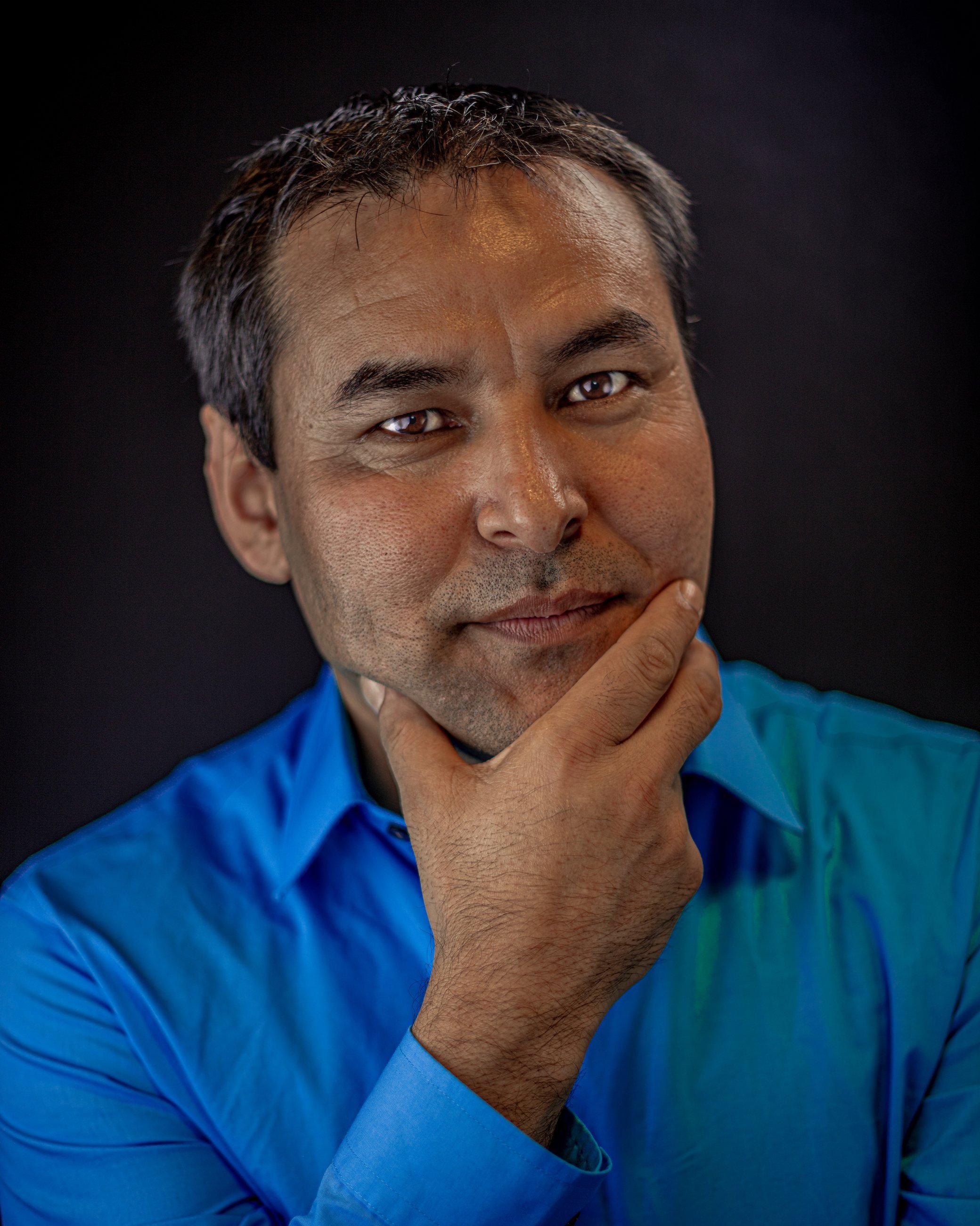 Studio portrait of a man in a blue shirt with his hand thoughtfully on his chin, portrait photography by Everlux Photo Co.