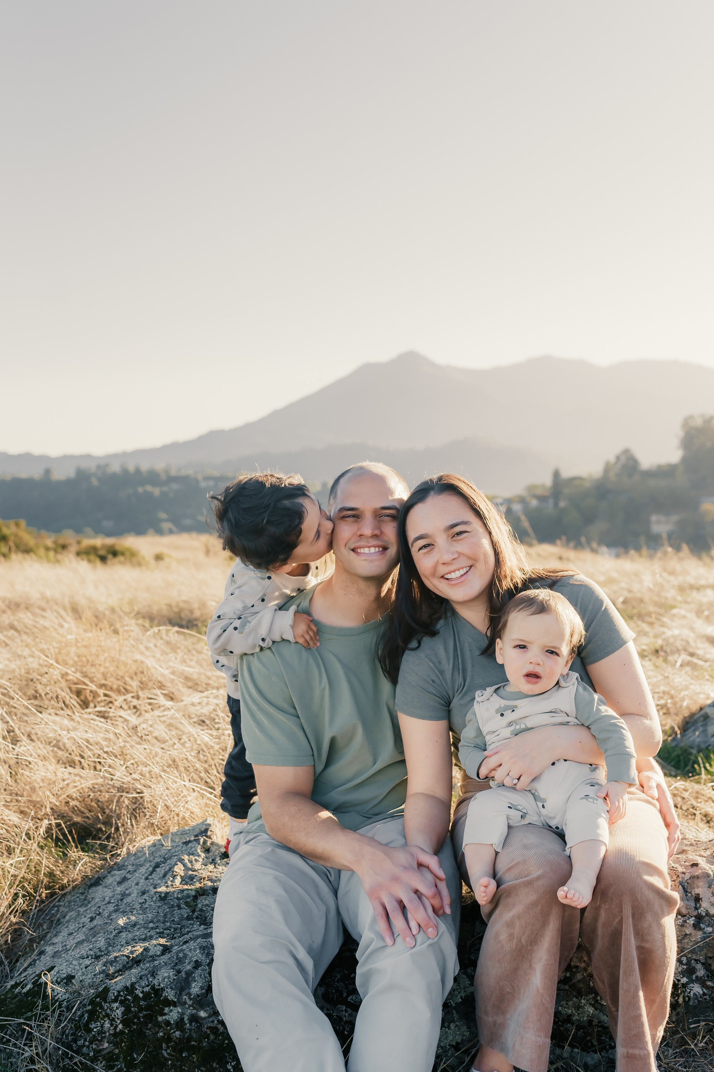 Candid family mini session photo in Marin County with parents and young children snuggling outdoors.jpeg