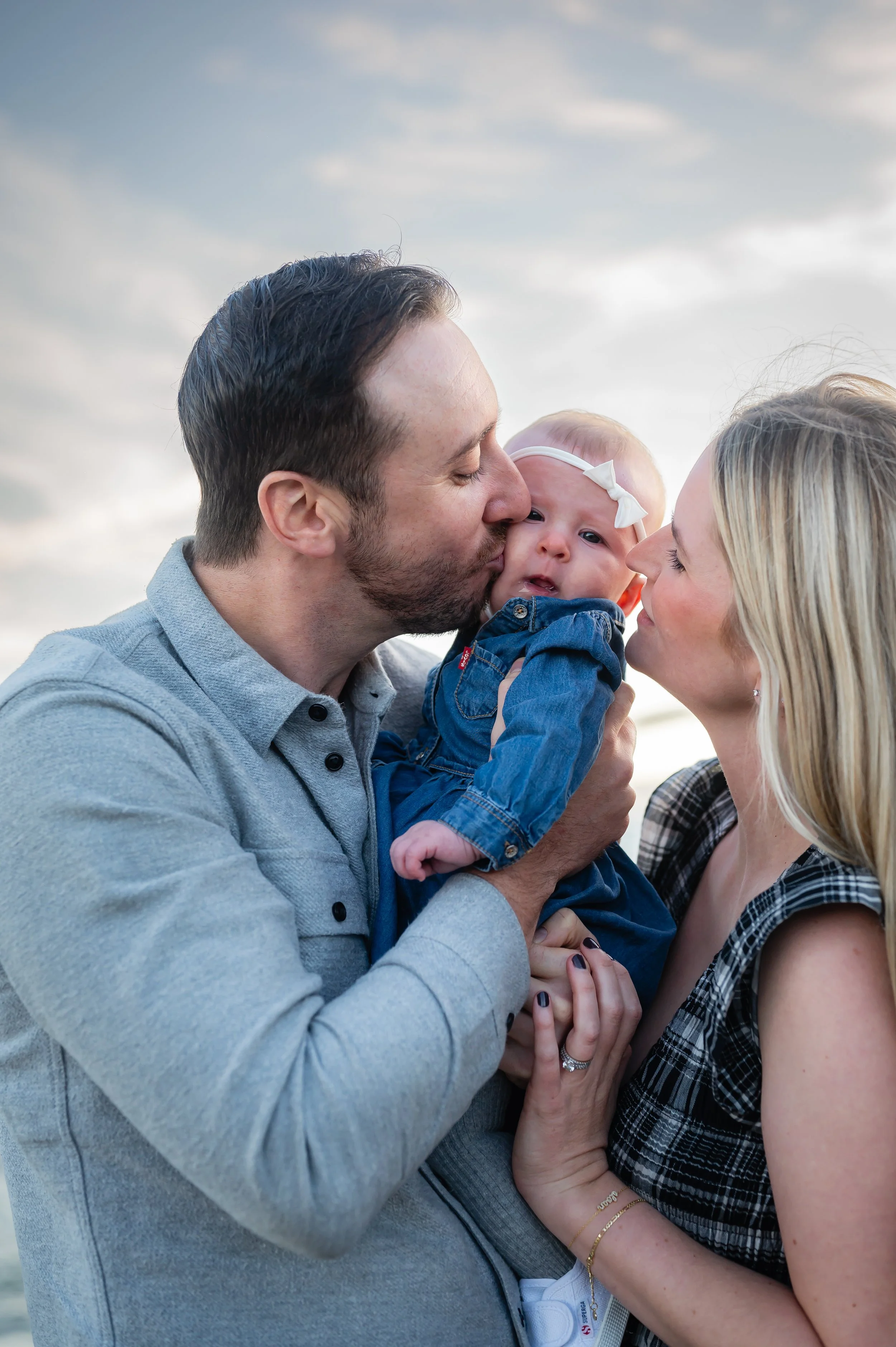 A man and woman kissing their baby girl outdoors during sunset.