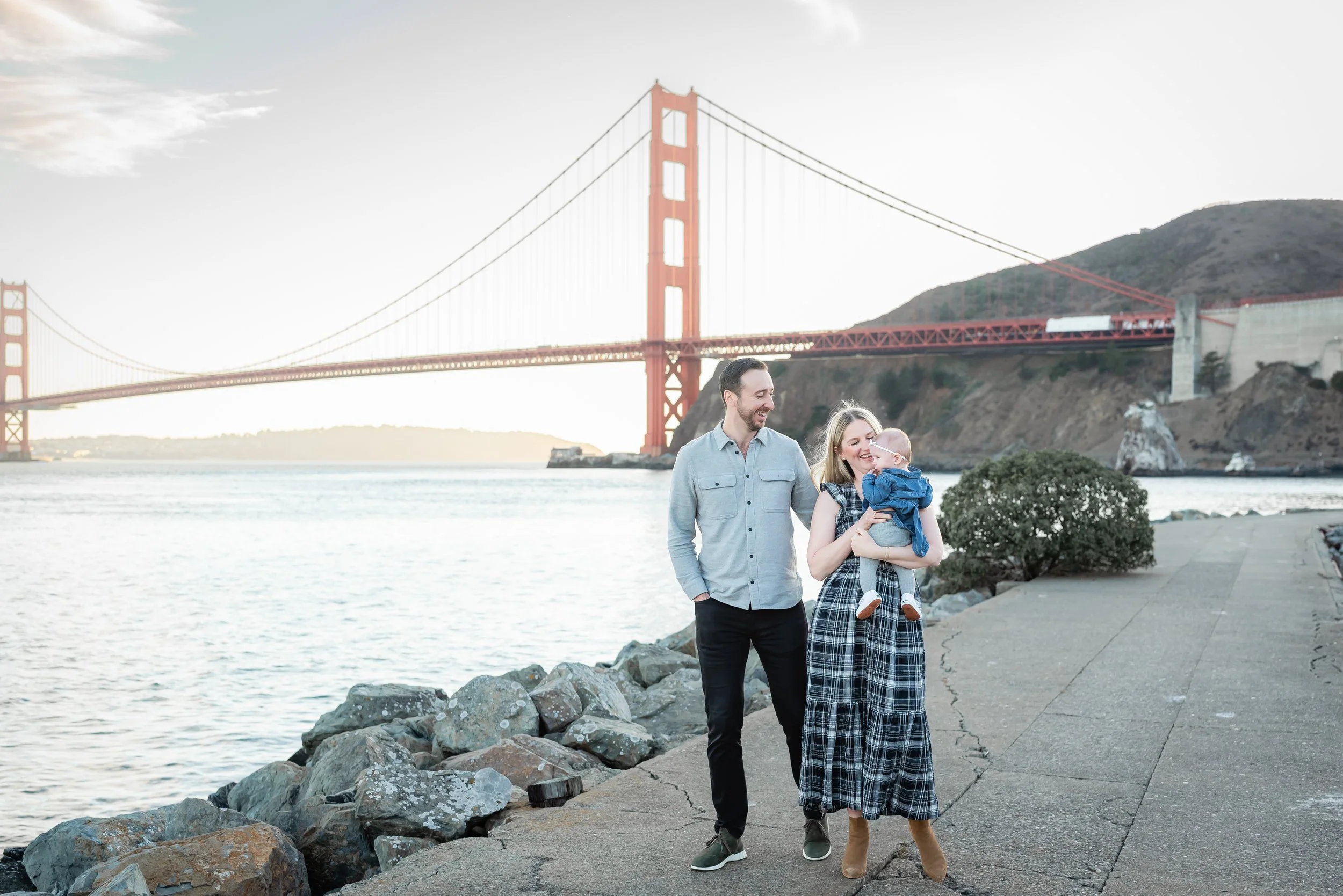 A family of three walking along a waterfront with the Golden Gate Bridge in the background.