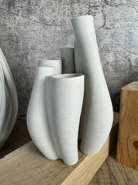 3D printed ceramic vase on a wooden surface against a textured wall.
