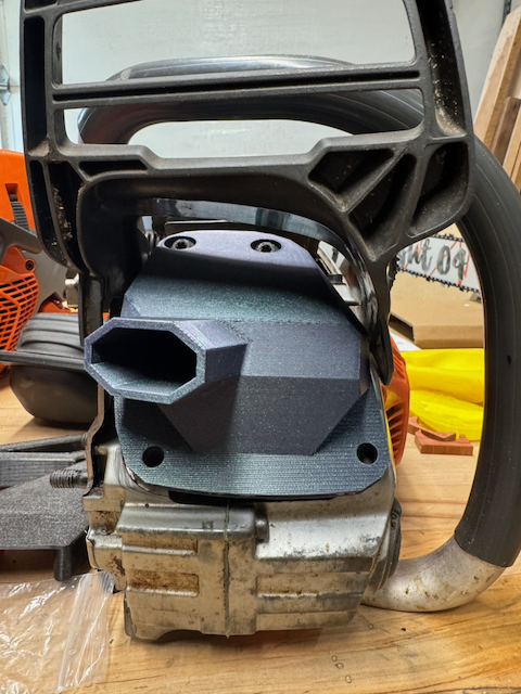 Close-up of a small engine, possibly for a chainsaw or leaf blower, placed on a wooden surface with parts and tools in the background.
