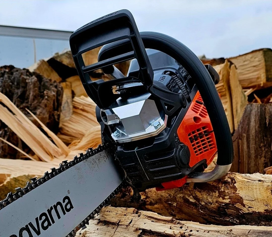 A chainsaw resting on chopped wood logs outdoors with a blue sky in the background.