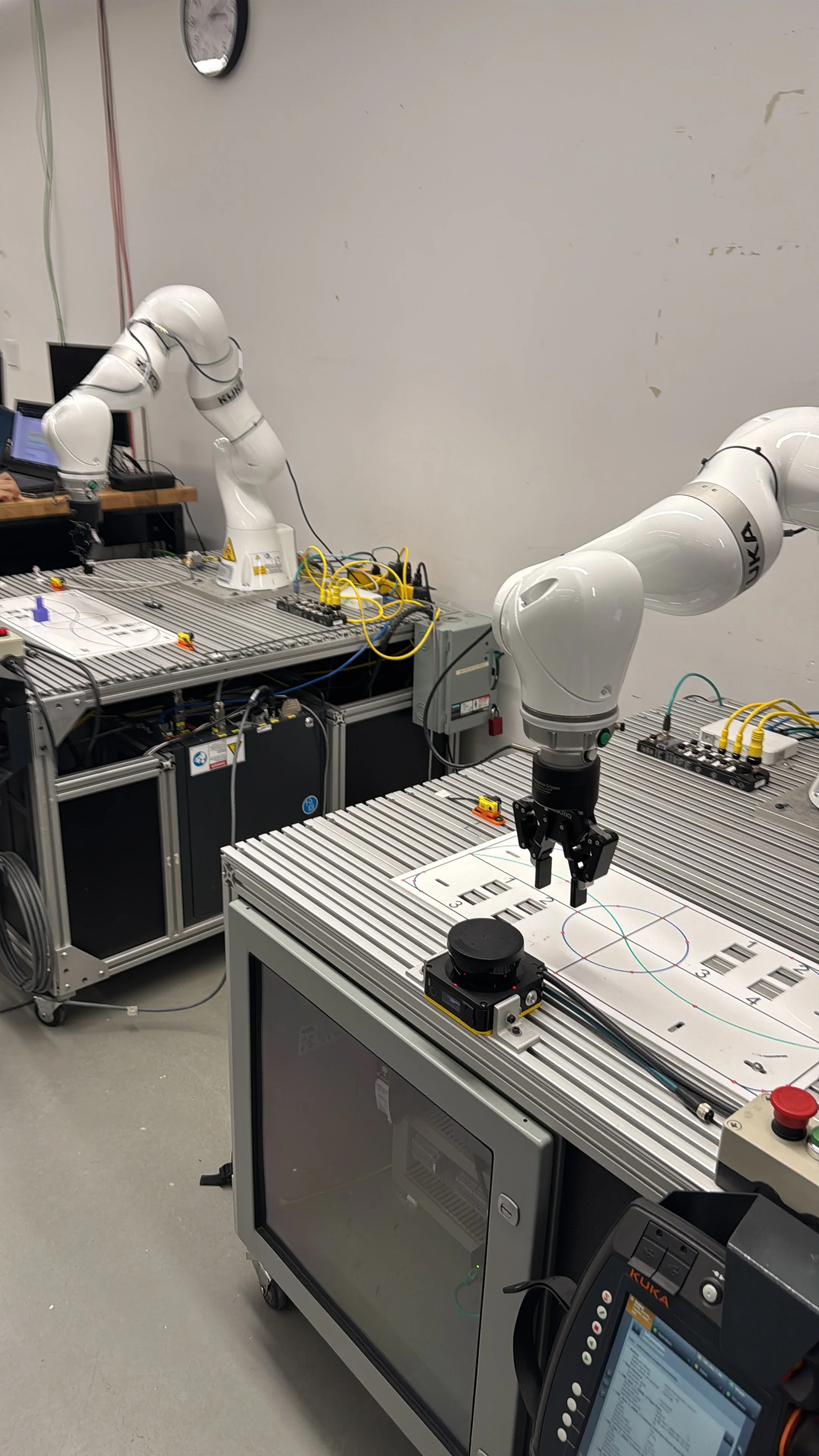 Laboratory with two robotic arms working on experiments or tasks, a microscope, a computer, and testing equipment on metal tables.