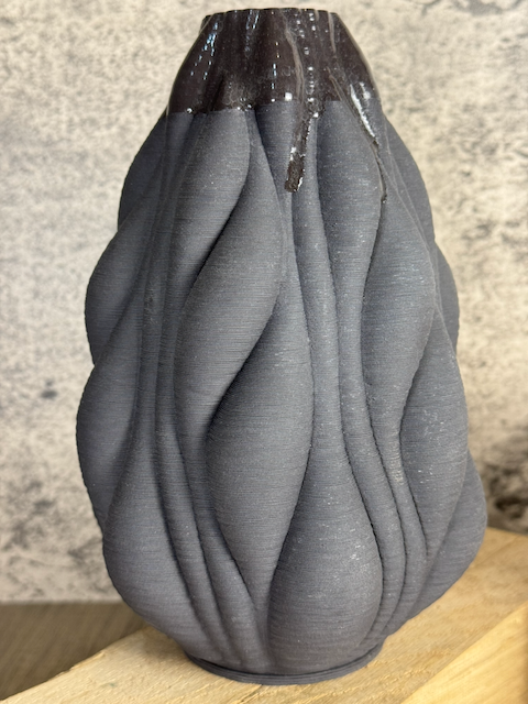 A black fabric vase with a textured, pleated design sitting on a wooden surface.