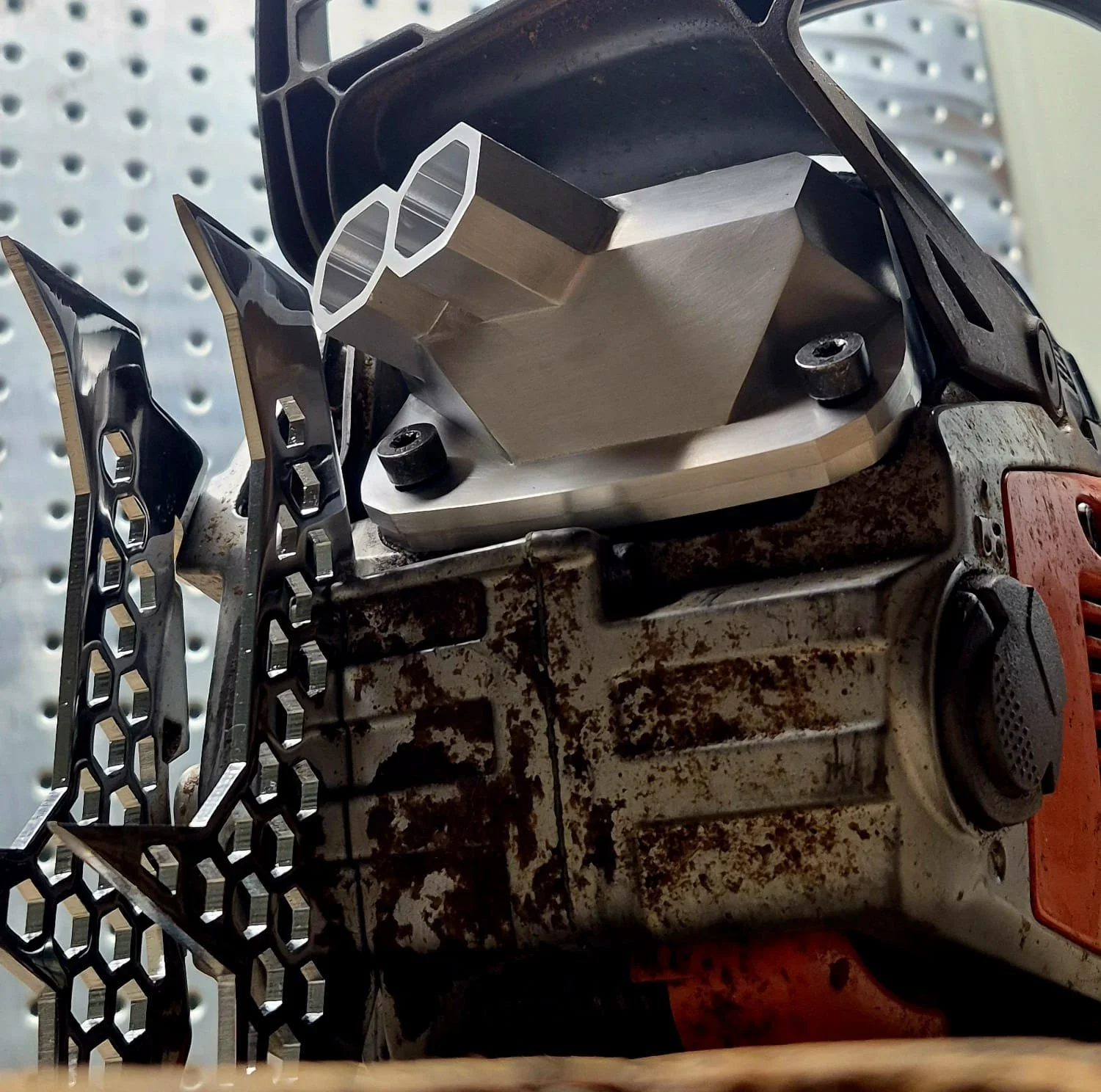 Close-up of a chainsaw with a rusty body, showing the guide bar and cutting chain, placed on a display shelf with a metal pegboard background.
