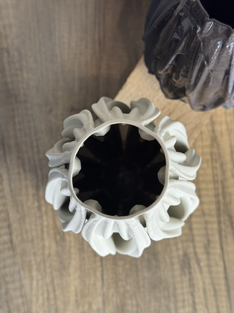 3D Printed ceramic vase with a white, ruffled, decorative cover around its opening, placed on a wooden surface.