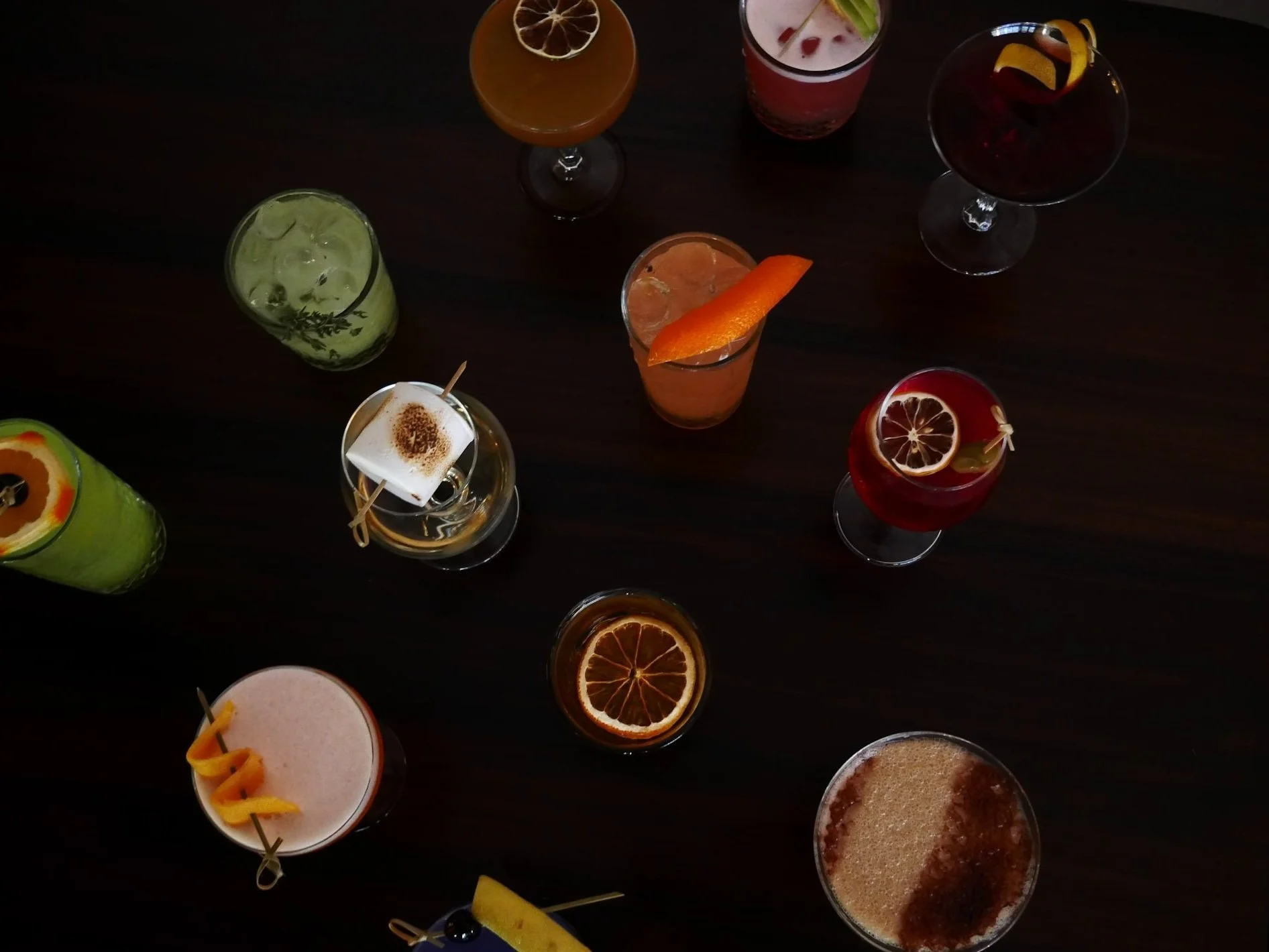 Various colorful cocktails and drinks on a dark table, garnished with fruit slices and decorations.