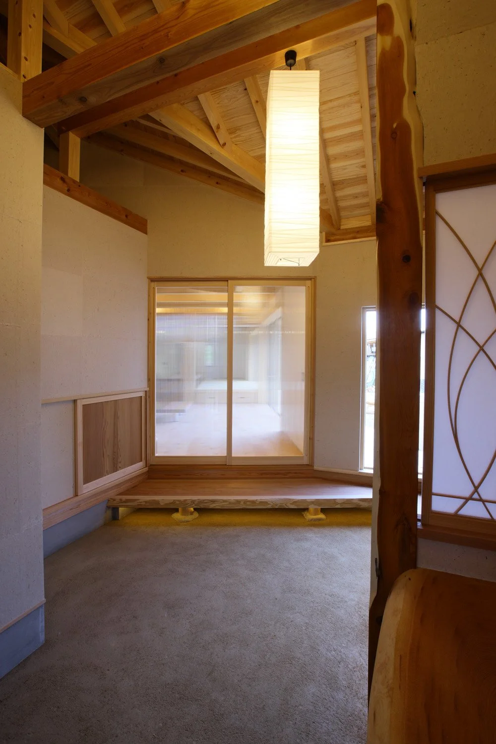 三和土土間に白い壁、木の屋根組が現れた玄関ホール。天井からは四角い長細い照明器具が吊り下げられている