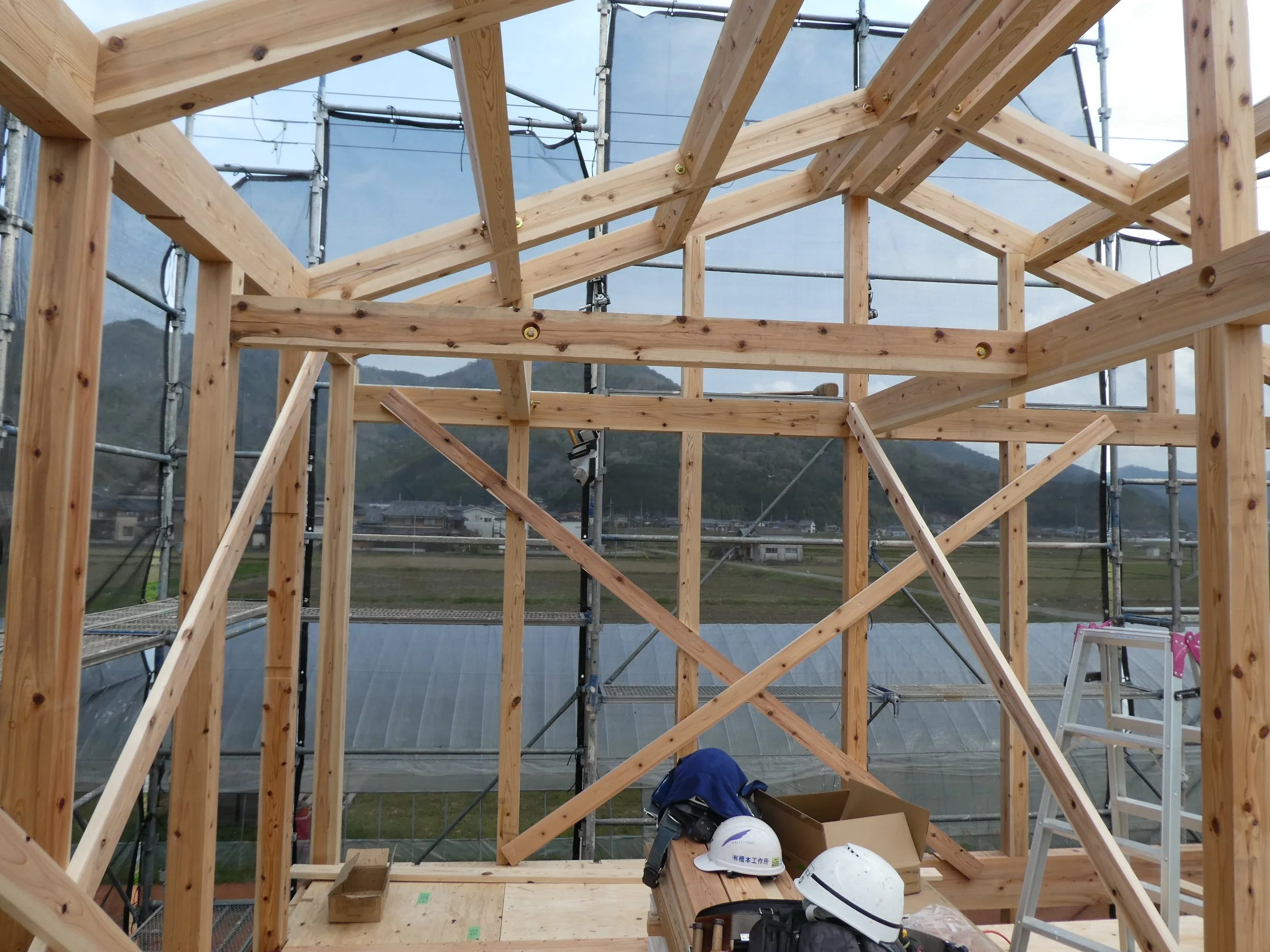 建築途中の木の骨組み。床に置かれた木材の上には幾つかのヘルメットが置かれている。