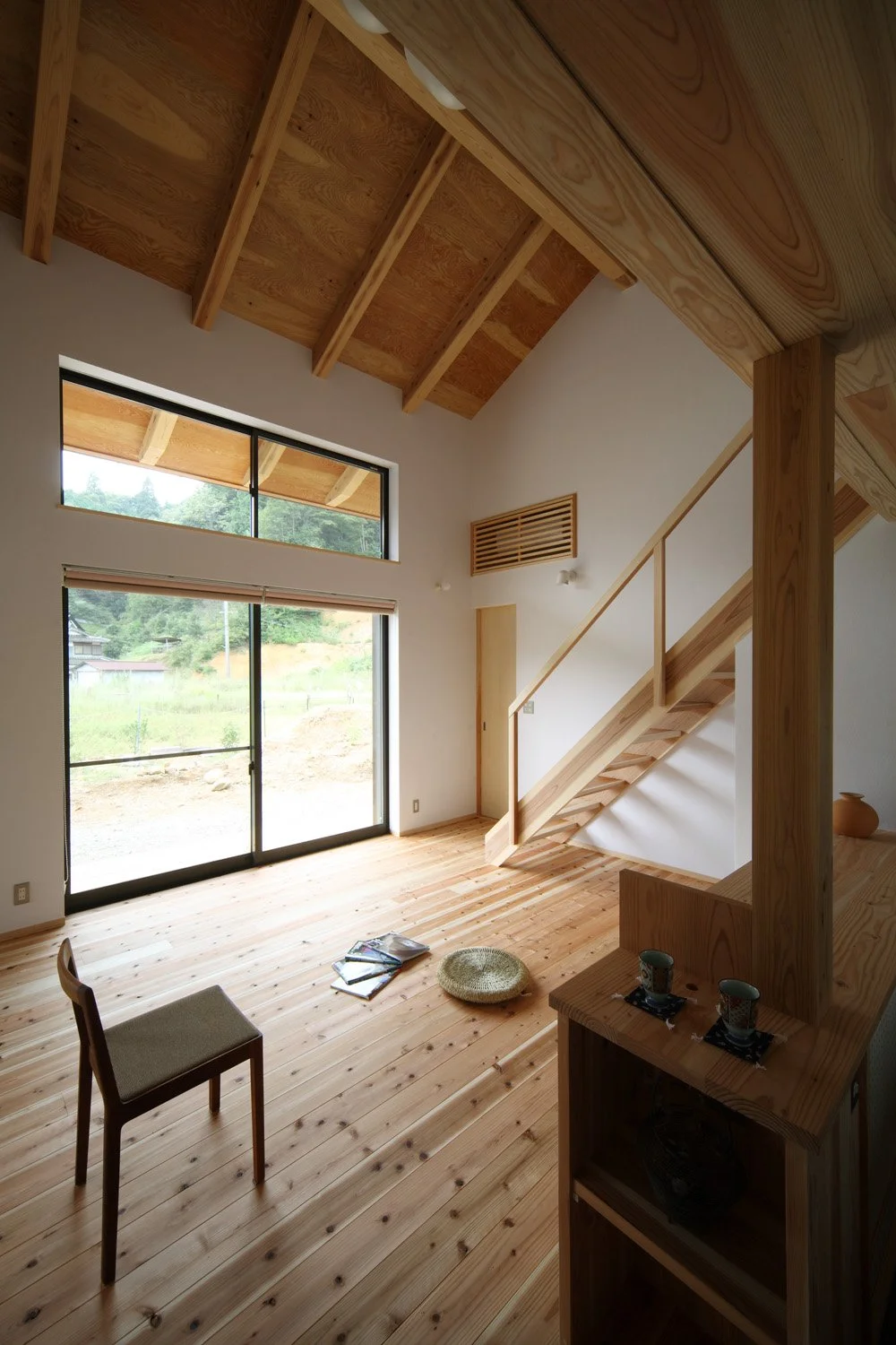 木の床と柱に梁、白い壁、２層吹抜の空間。正面の壁には上下２段の窓があり、外の景色が見えています。木の階段が左から右へ向かって登っている