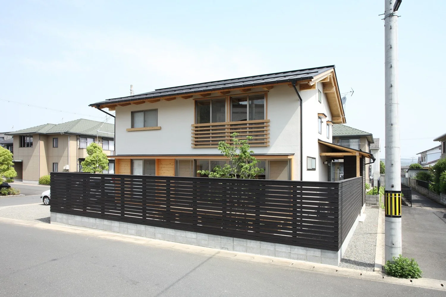 黒い板塀の中に建つ白い２階建ての切妻屋根の家