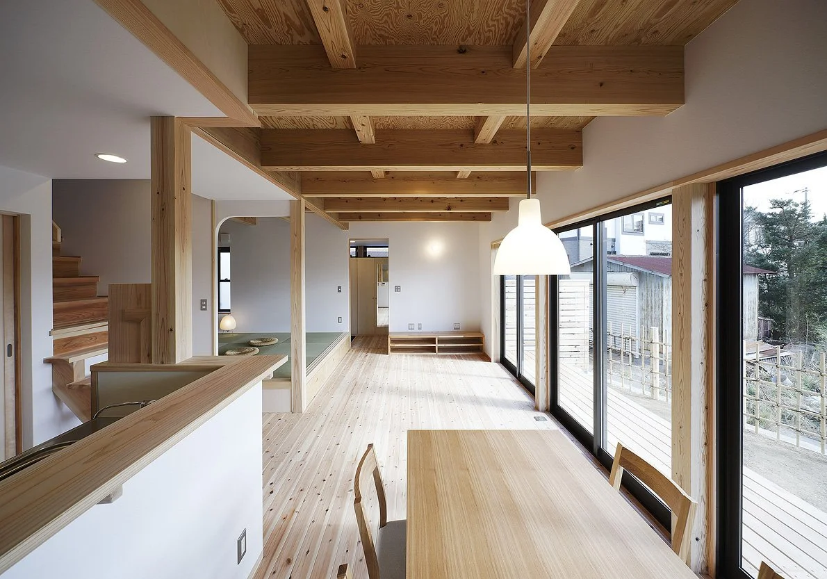 木の床と天井に白い壁。端には木のテーブルと椅子が置かれていて部屋の奥にはテレビ台があり、その左側には小上がりがある。