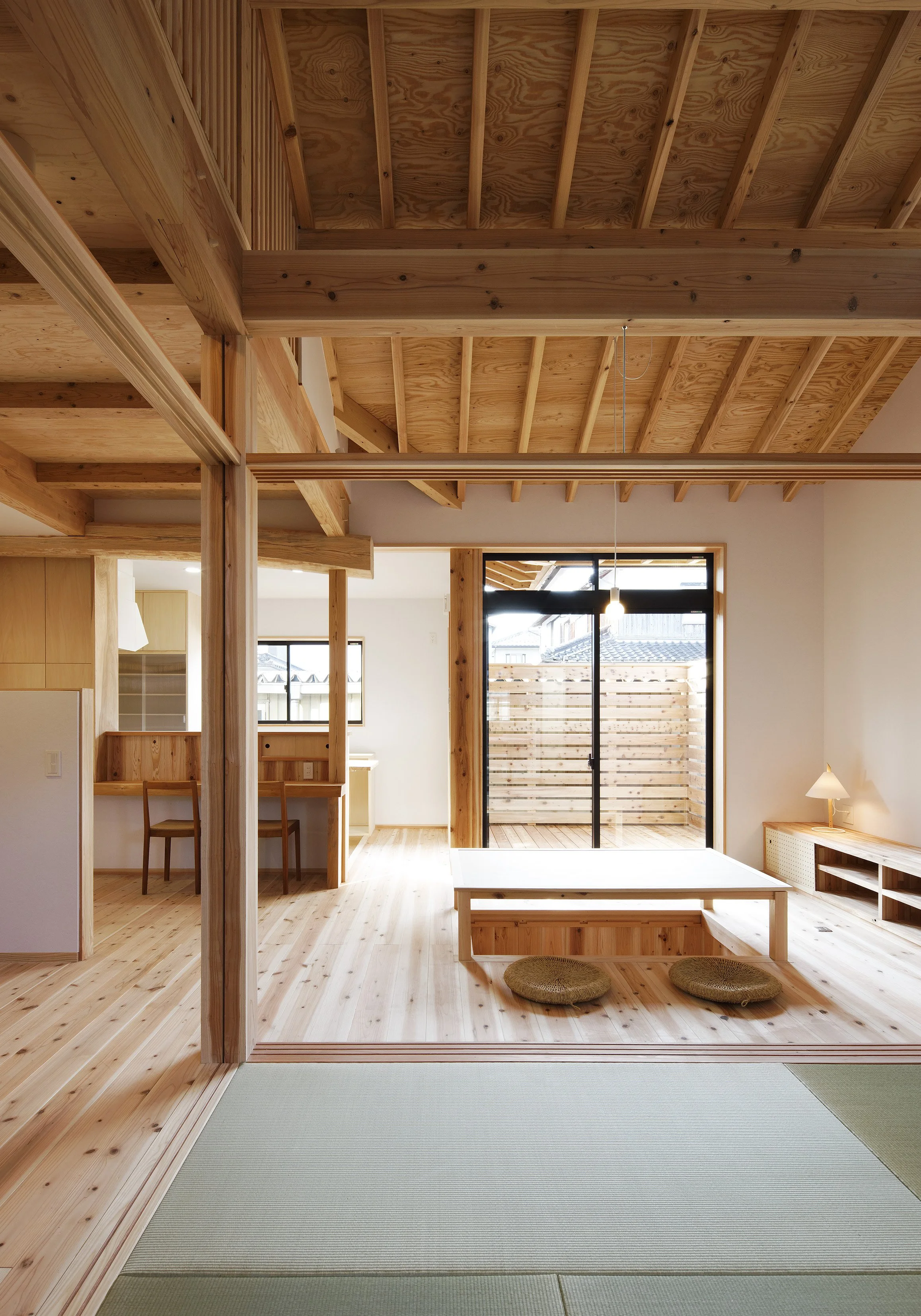 木の床に柱と白い壁。部屋の右手には掃き出し窓があってその左手はカウンターがあり、その奥には腰高窓がある。カウンターの前には２脚の椅子があり、掃き出し窓の前には掘り炬燵式の座卓が置かれている。