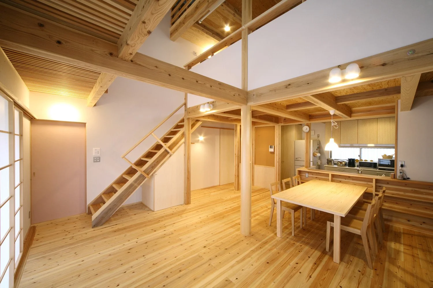 木の床と柱に梁、白い壁で２層吹き抜けた空間部屋の片隅には木の椅子とテーブルが置かれ、カウンターの奥にはキッチンがある