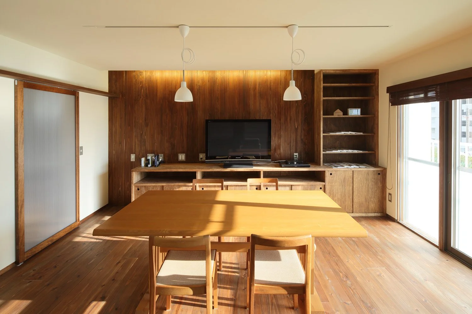 部屋の中心に置かれたテーブルとその奥にカウンターがありテレビが置かれている。窓からは陽射しが射し込み明るい室内