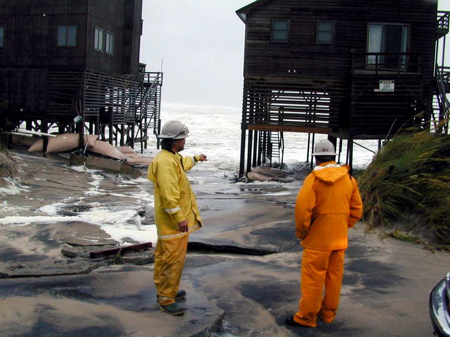 Nags Head, N.C., 8/1/99 -- Ocean overwashes flushed between coastal homes, ripping up their roadways. The change of direction by Dennis brought high seas and winds that battered and flooded the coastal road. Here, crew from NC Power(L) and Virginia Power(R) check the threat of live lines leading to the homes. Photo by DAVE GATLEY/FEMA News Photo Photo by Dave Gatley - Jul 31, 1999 - Location: Nags Head, NC