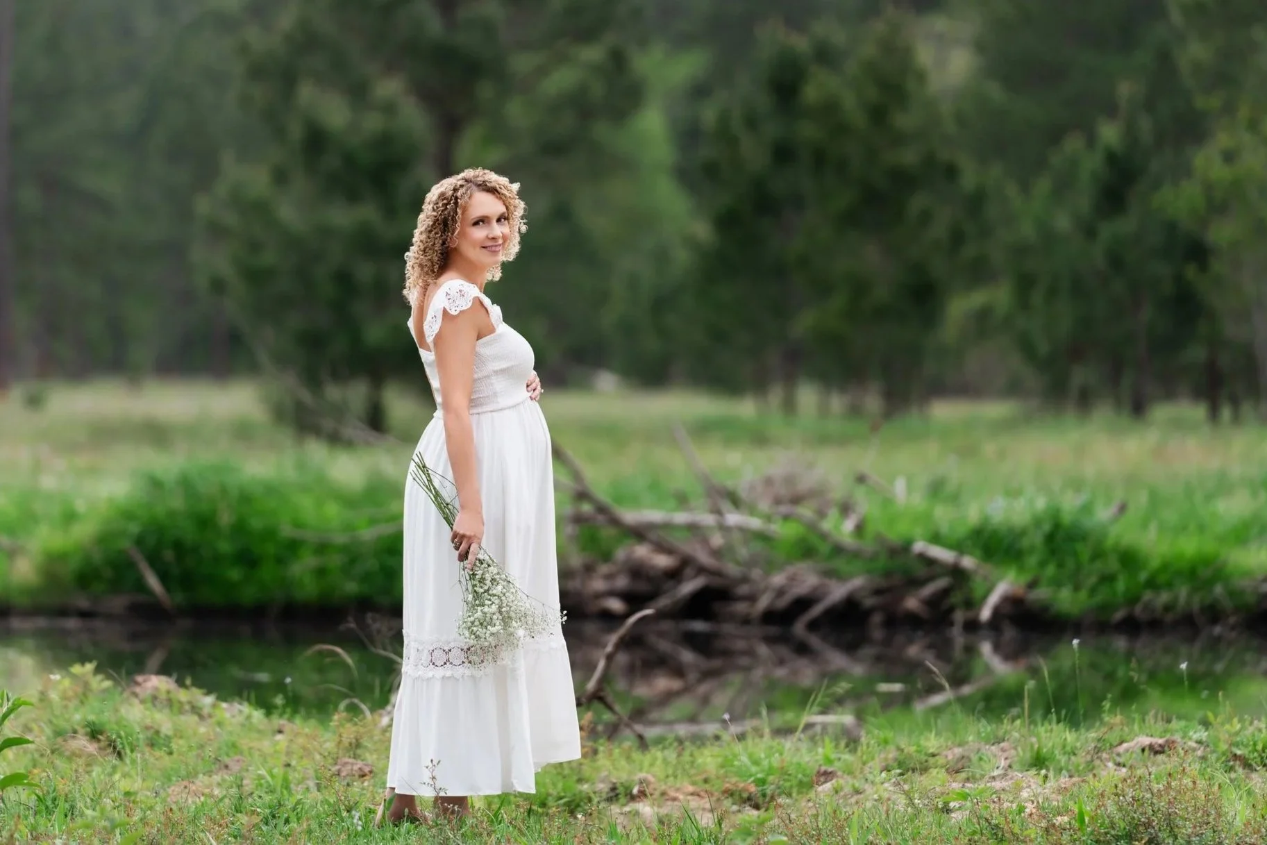 mom-to-be holding flowers standing by pond in woods