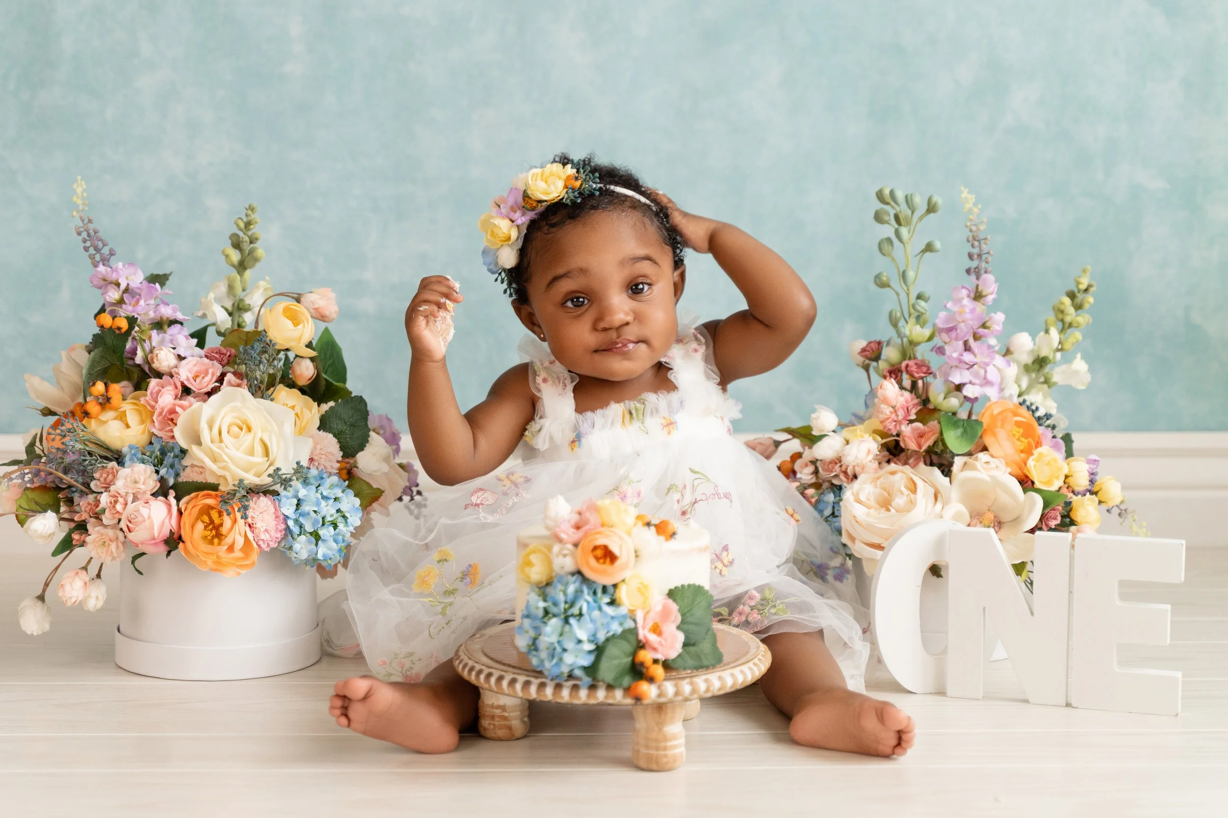 One-year-old Ava sitting in front of a floral cake smash setup, showing playful expressions during her session in Cypress, Texas.