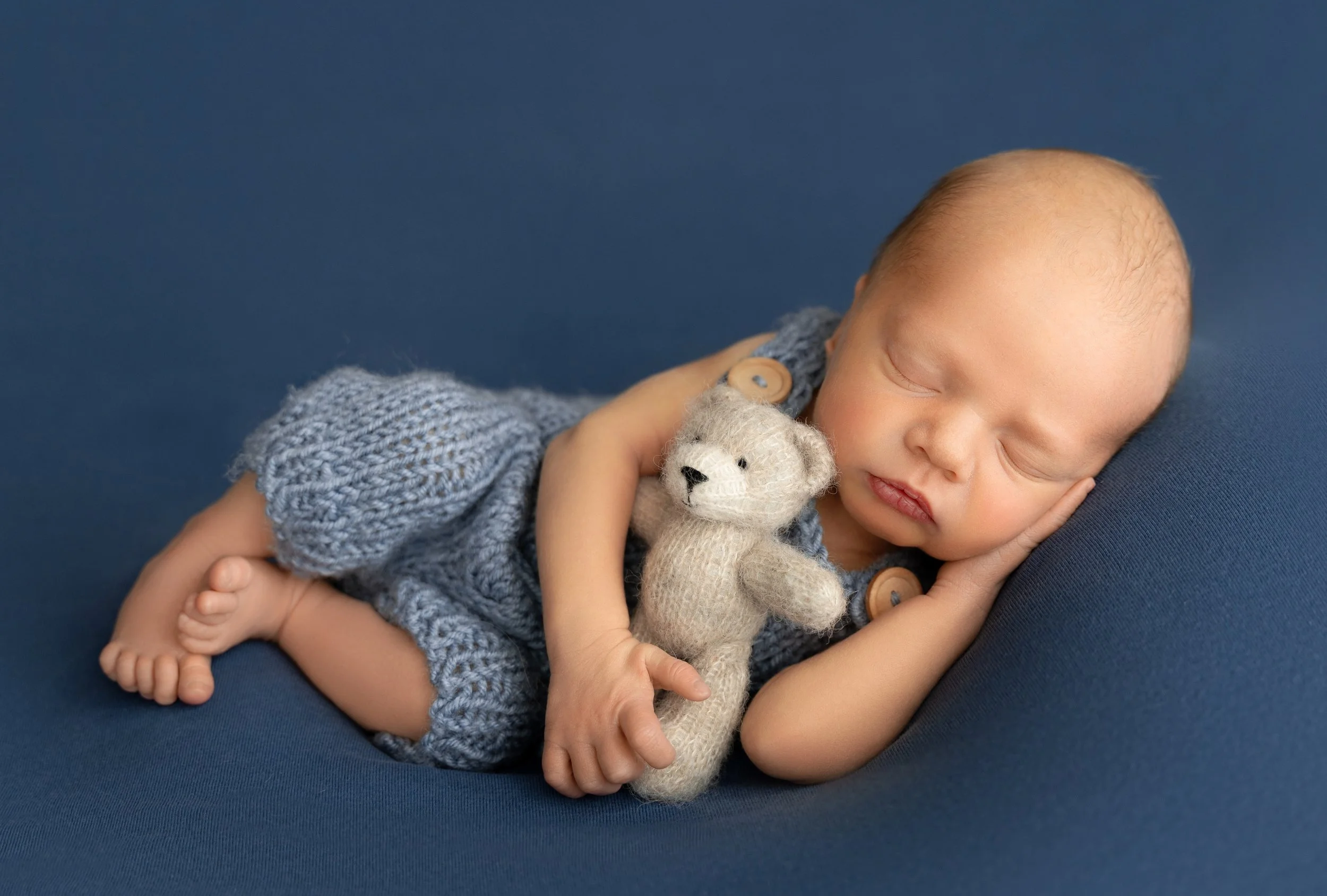 newborn Nolan dressed in blue and holding a tiny teddy bear