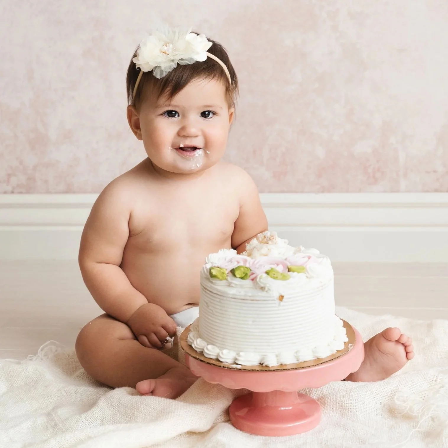 Smiling one-year-old celebrating her first birthday during a cake smash photography session with frosting-covered cheeks.