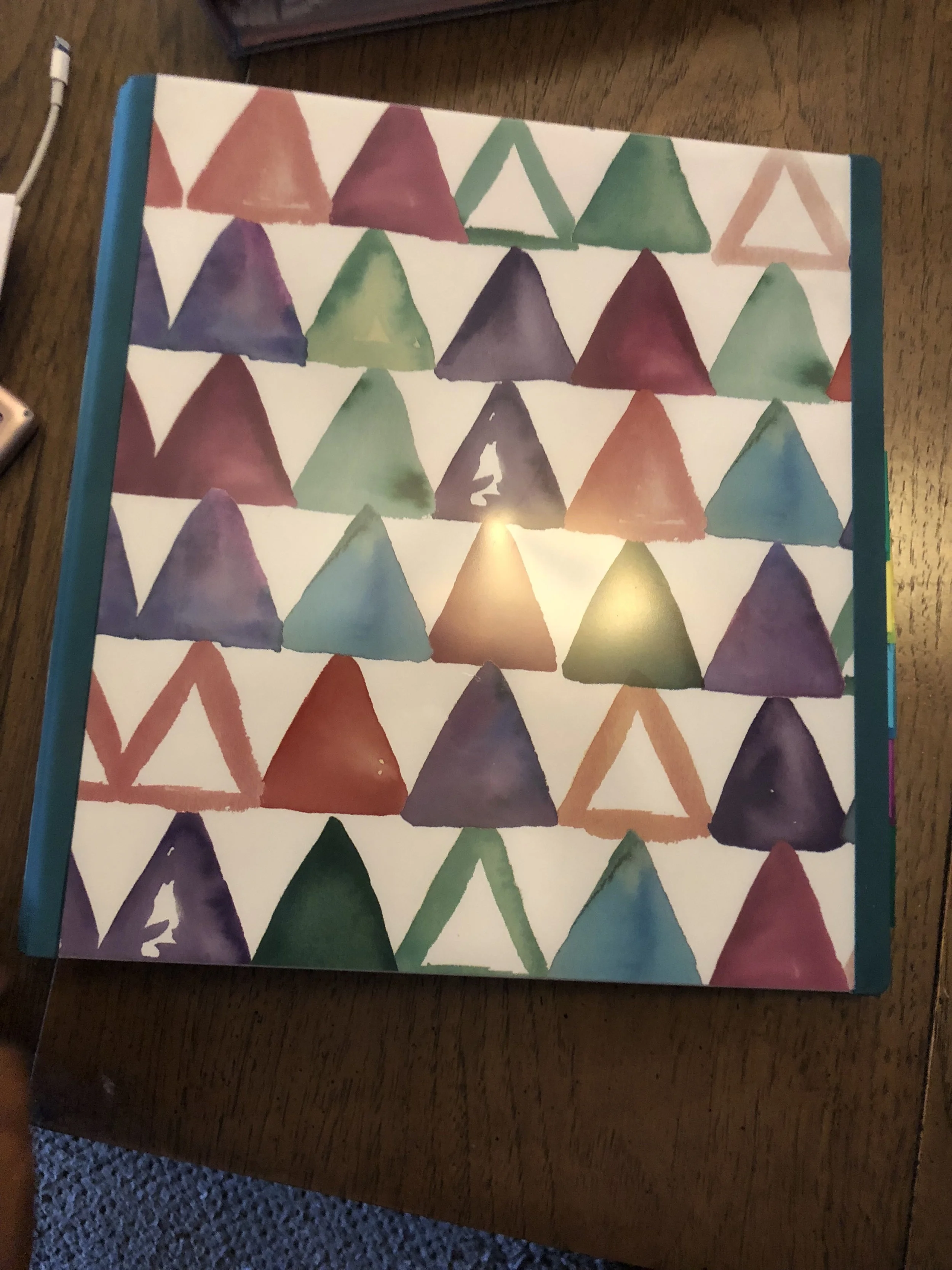 Caption: I purchased this binder Staples. It has the capacity to hold 400 sheets of paper, which should carry me for a long time before I need to add a second binder. Most Office Supply stores have really beautiful options. I also like this binder because it has a lot of symbolism with the triangle. It is the elemental symbol for fire. When turned upside down it becomes the symbol for water. The colors represent fire and the upside down triangles (the white space) represents water. Triangles are also the strongest shape.