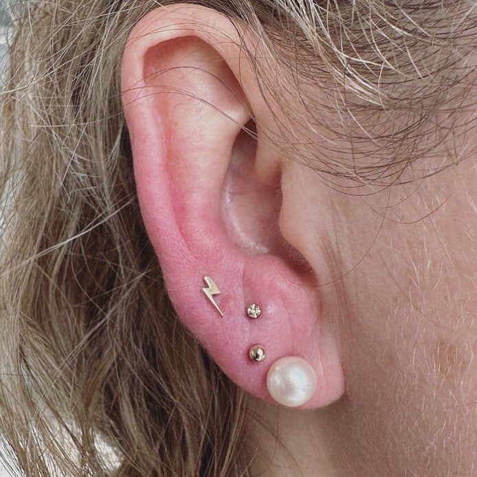 @mannus_stabbings nailed this little lobe cluster! 🖤 three fresh stacked lobes 🖤 her client chose the lightening bolt from @junipurrjewelry ✨ a hammered disk from @alchemyadornment ✨and a gold bead from @buddhajewelryofficial ✨ all in solid 14k yel