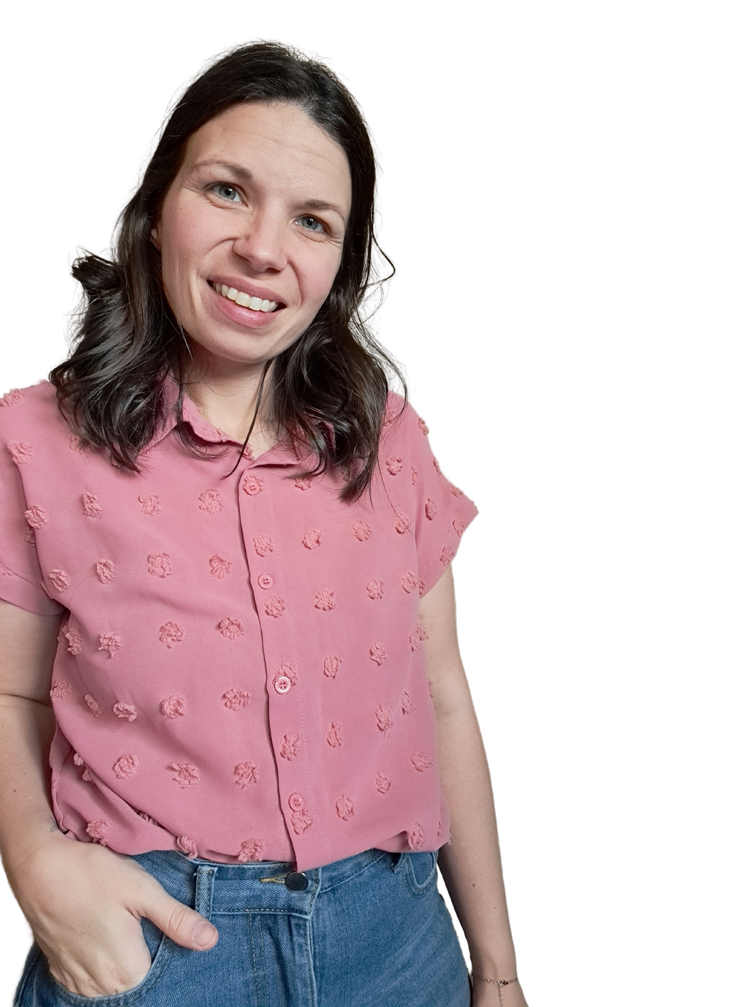 A woman with dark brown hair wearing a pink button-up shirt with textured circular patterns and blue jeans, smiling and posing with her left hand in her pocket.