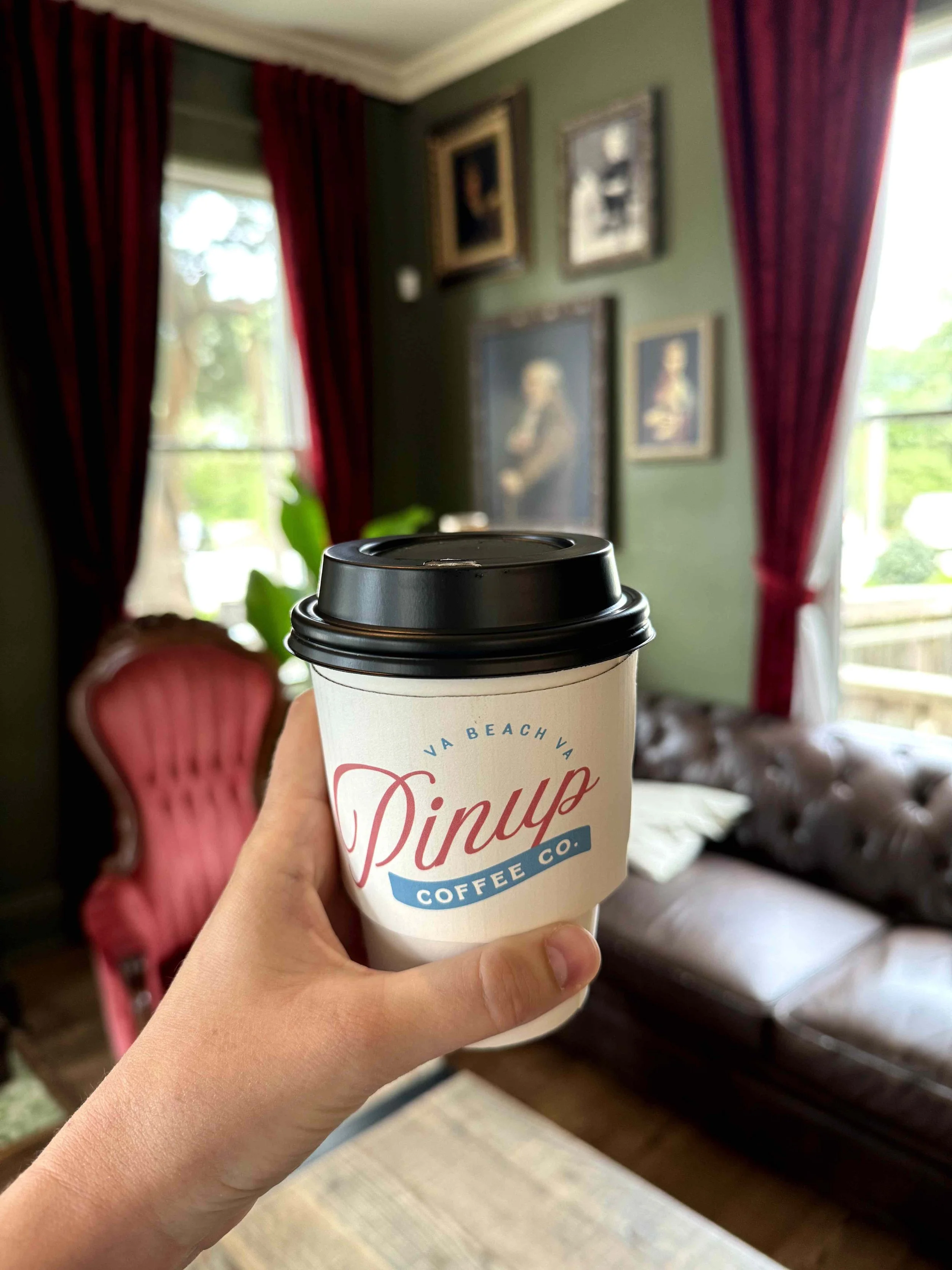 Pinup Coffee to-go cup held up inside of old house