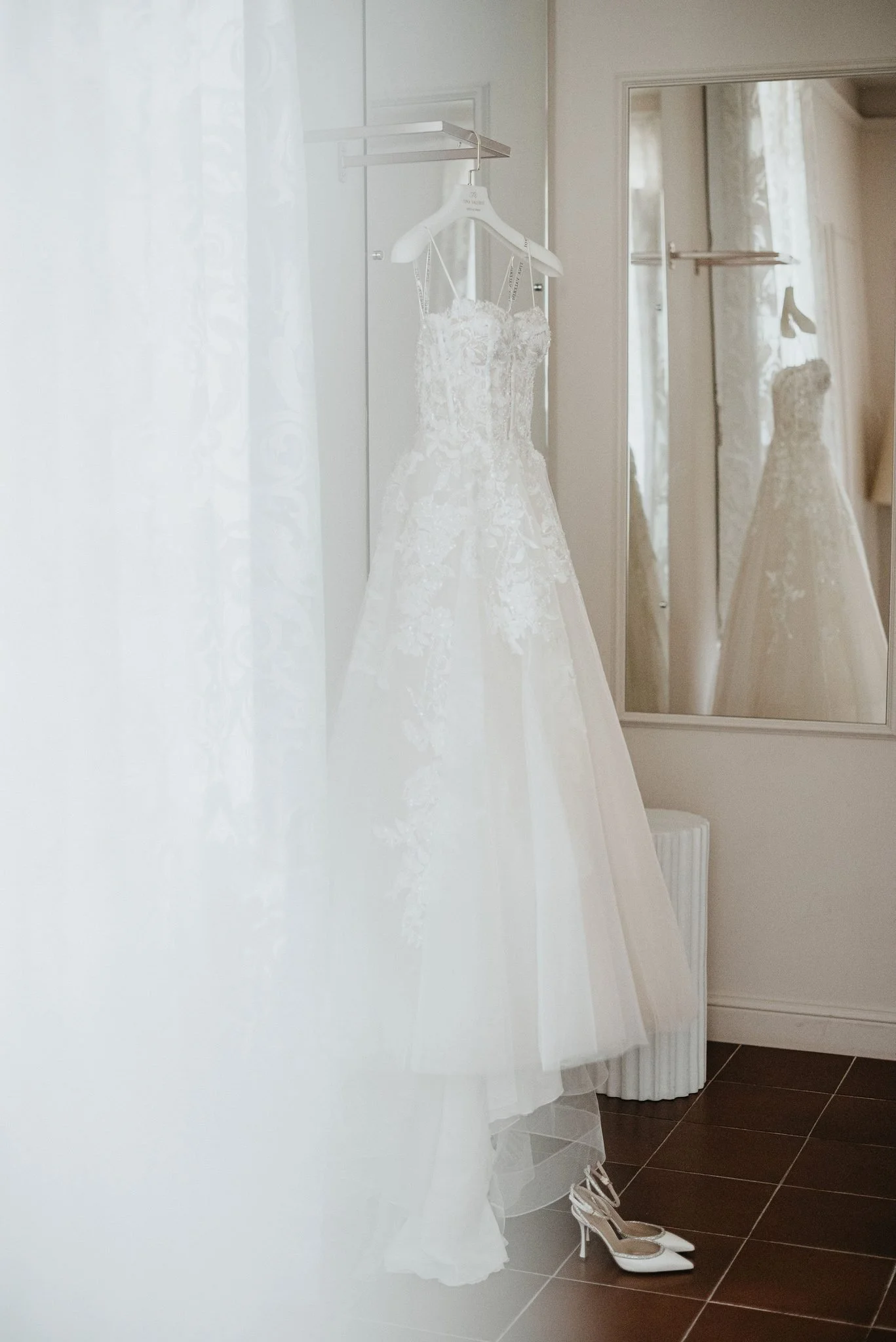 Abito da sposa bianco appeso vicino alla finestra, con le scarpe posate a terra.