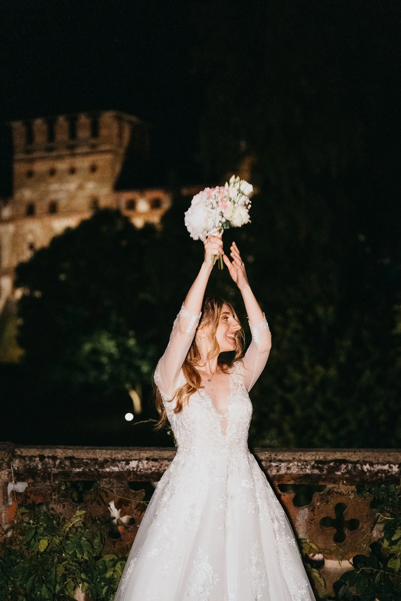 La sposa lancia il bouquet di sera davanti alla facciata illuminata del castello di Piovera