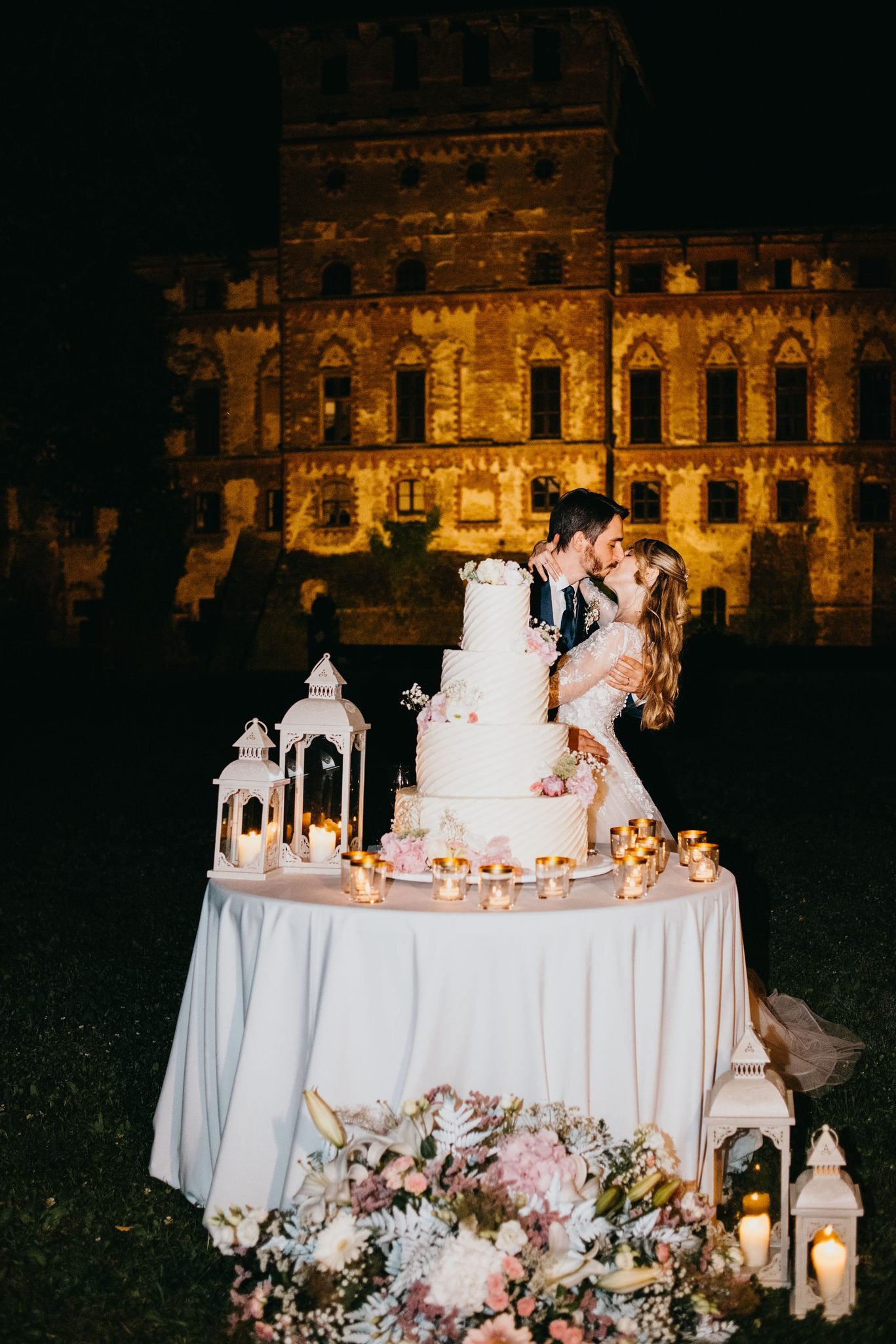Gli sposi tagliano la torta a più piani davanti al Castello di Piovera illuminato.