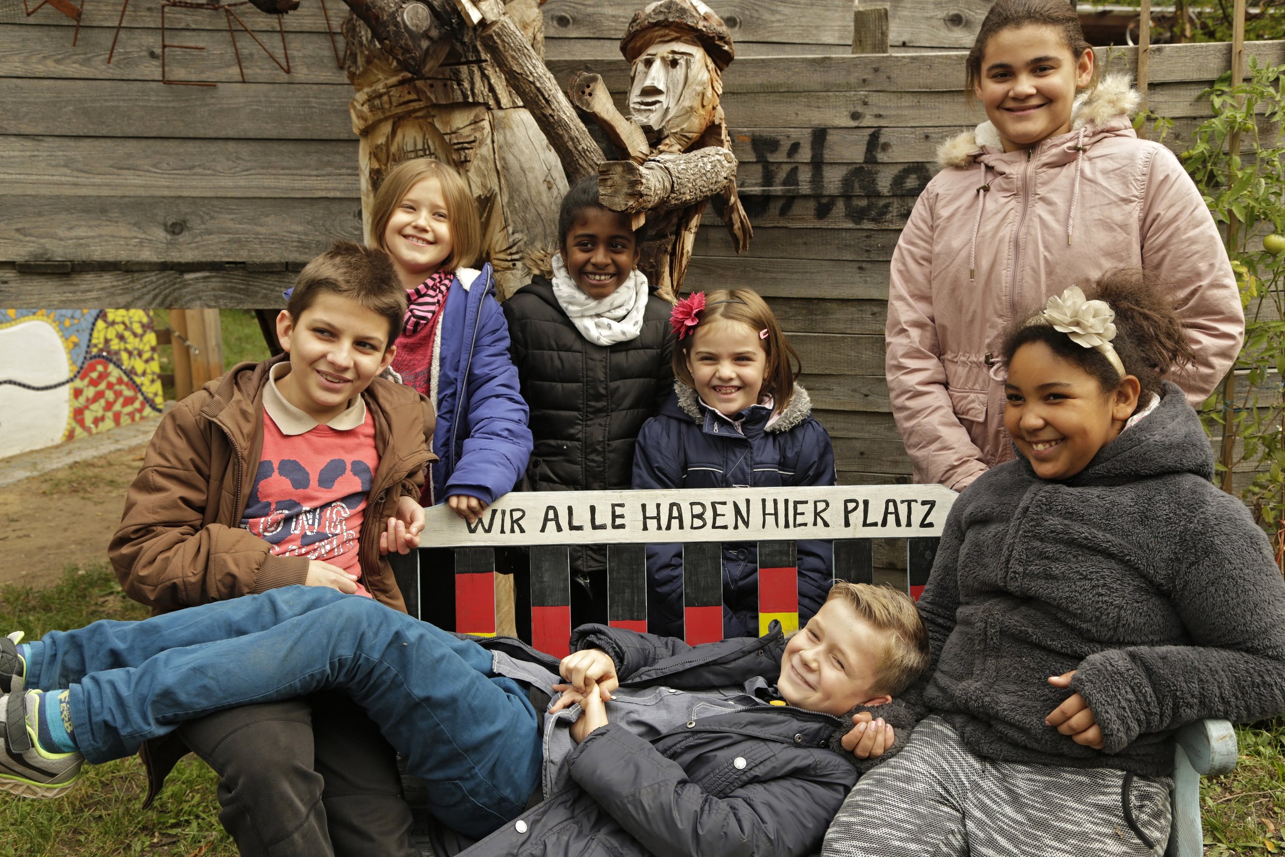 Bild aus dem Programm CHILDREN Entdecker (Kinderarmut): Kinder unterschiedlicher Herkunft sitzen auf einer Bank mit der Aufschrift "Wir alle haben hier Platz"