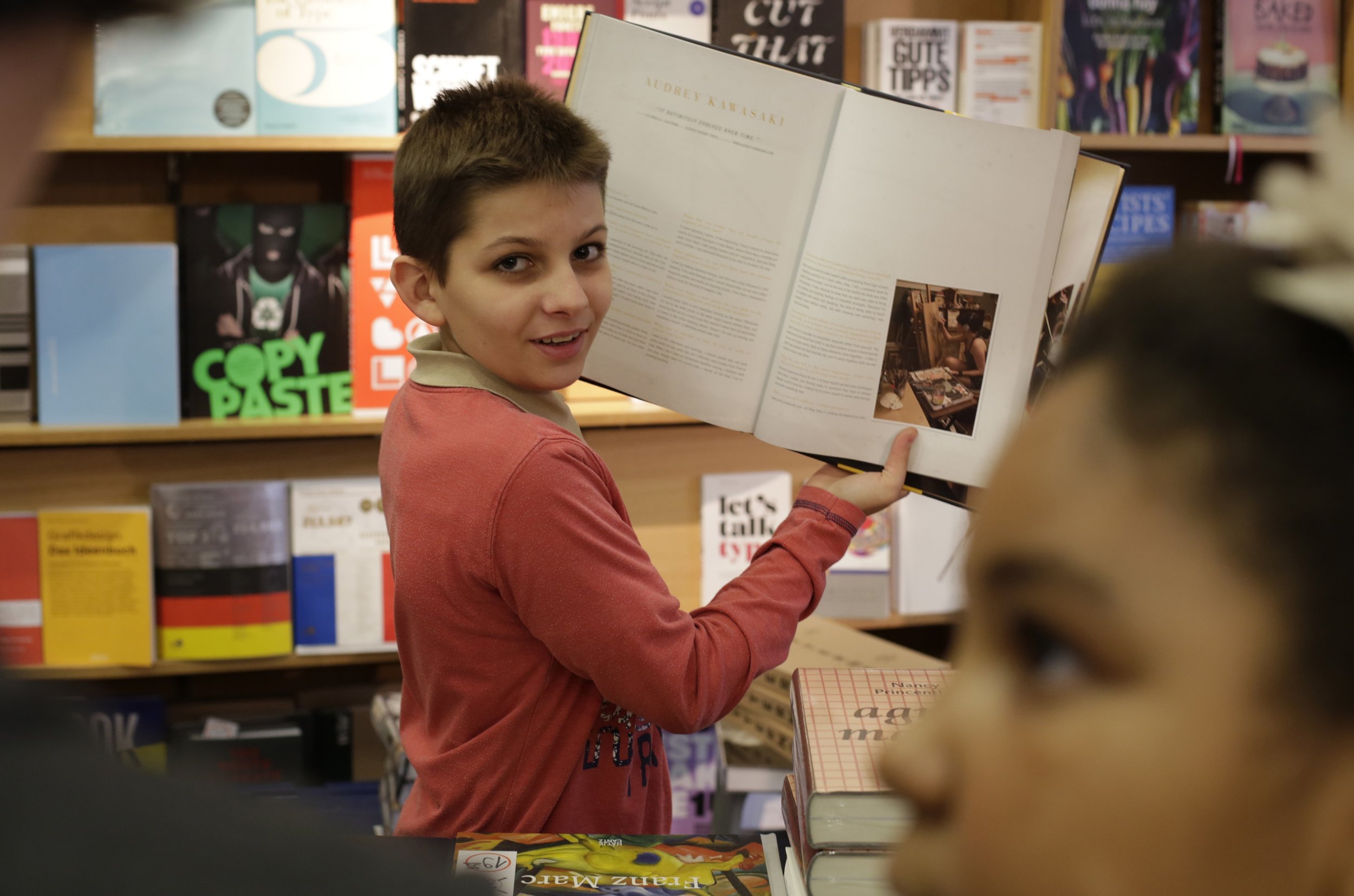Bild aus dem Programm CHILDREN Entdecker (Kinderarmut): Junge steht vor einem Bücherregal und hält ein Buch in den Händen