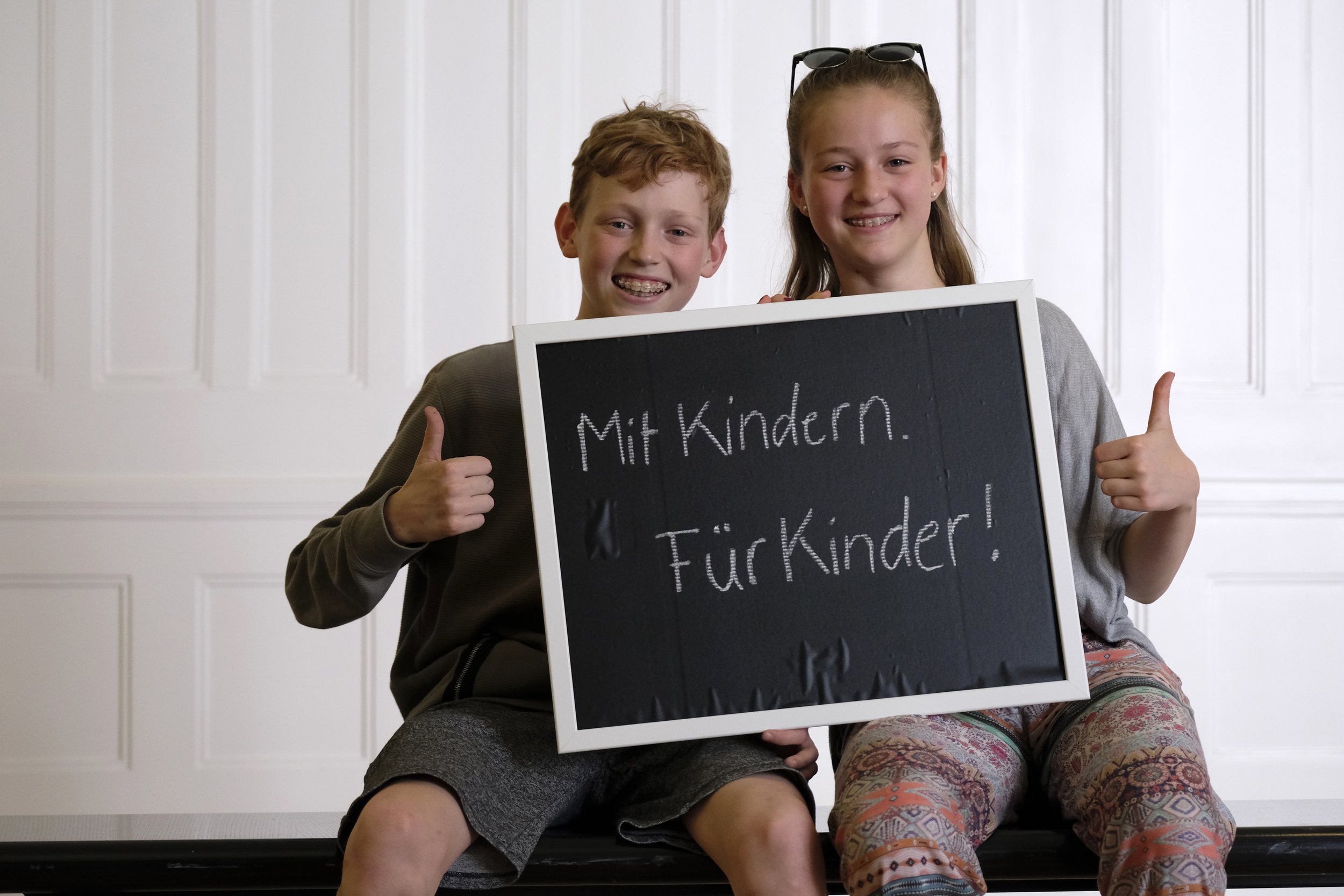 Bild vom CHILDREN Kinderbeirat (Partizipation): Junge und Mädchen halten ein  hoch, auf dem steht "Mit Kindern. Für Kinder!", beide halten den Daumen nach oben