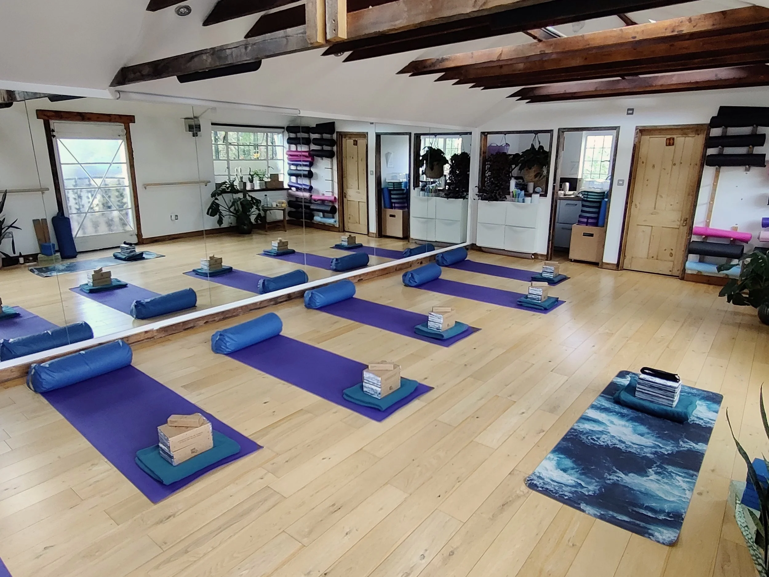Studio Space at Training Points. Bright studio in renovated barn with wooden floors and high ceilings, there are two windows and glass door, small kitchen space and lots of plants. Yoga mats with bolsters and blocks are laid out.